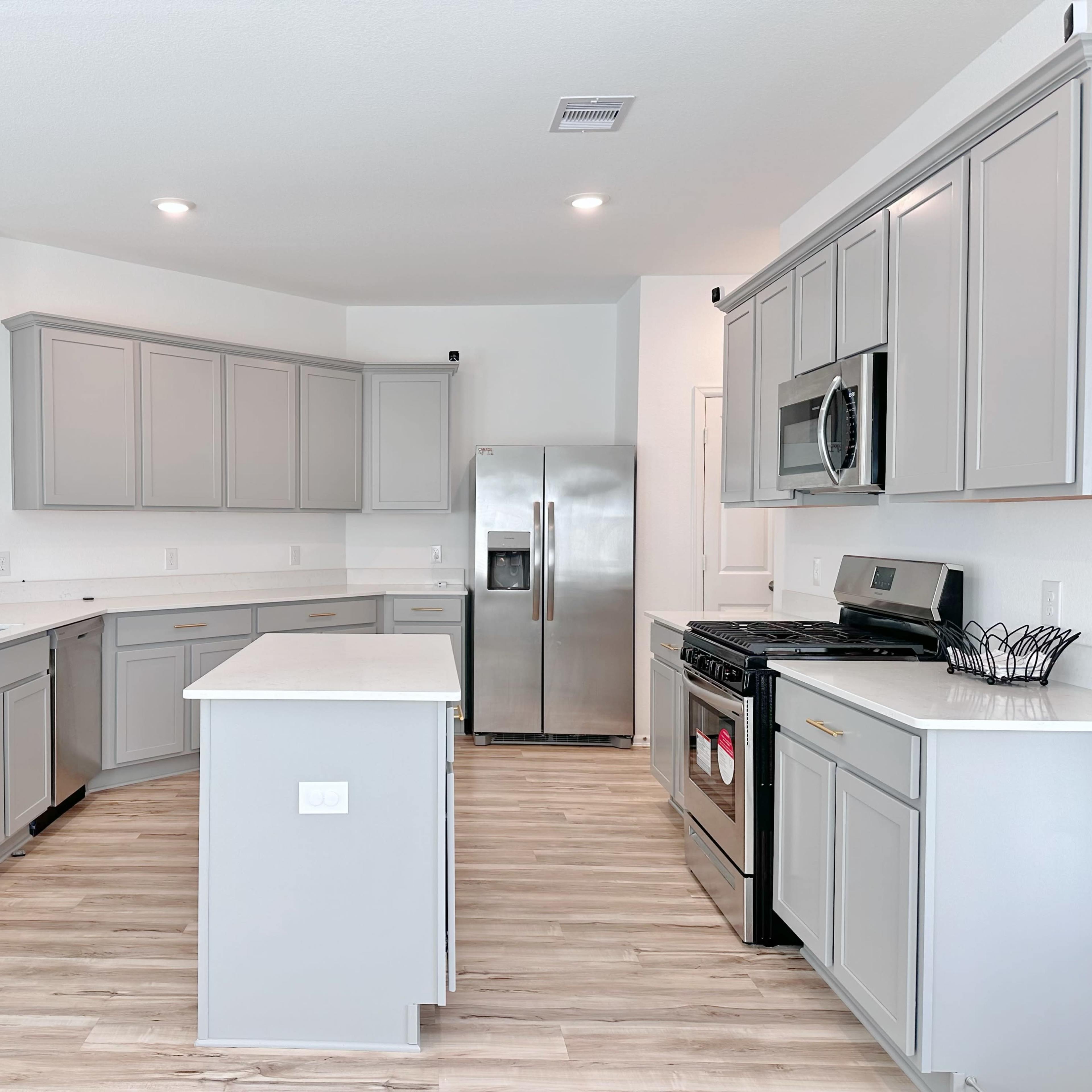 A modern kitchen with light gray cabinets, white countertops, stainless steel appliances, and a spacious layout.