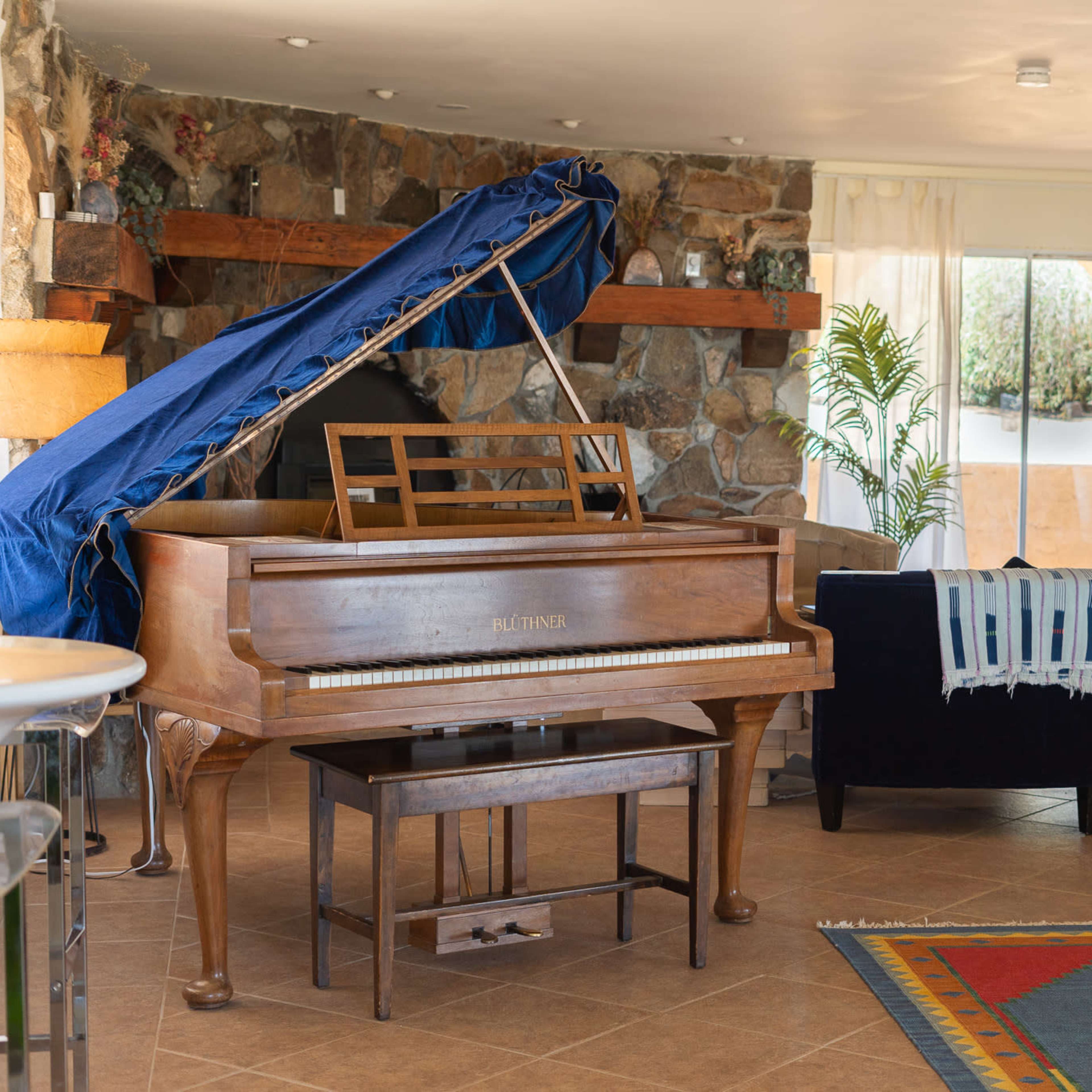 A spacious living area featuring a piano, a blue couch, and stone walls, with large windows letting in natural light.