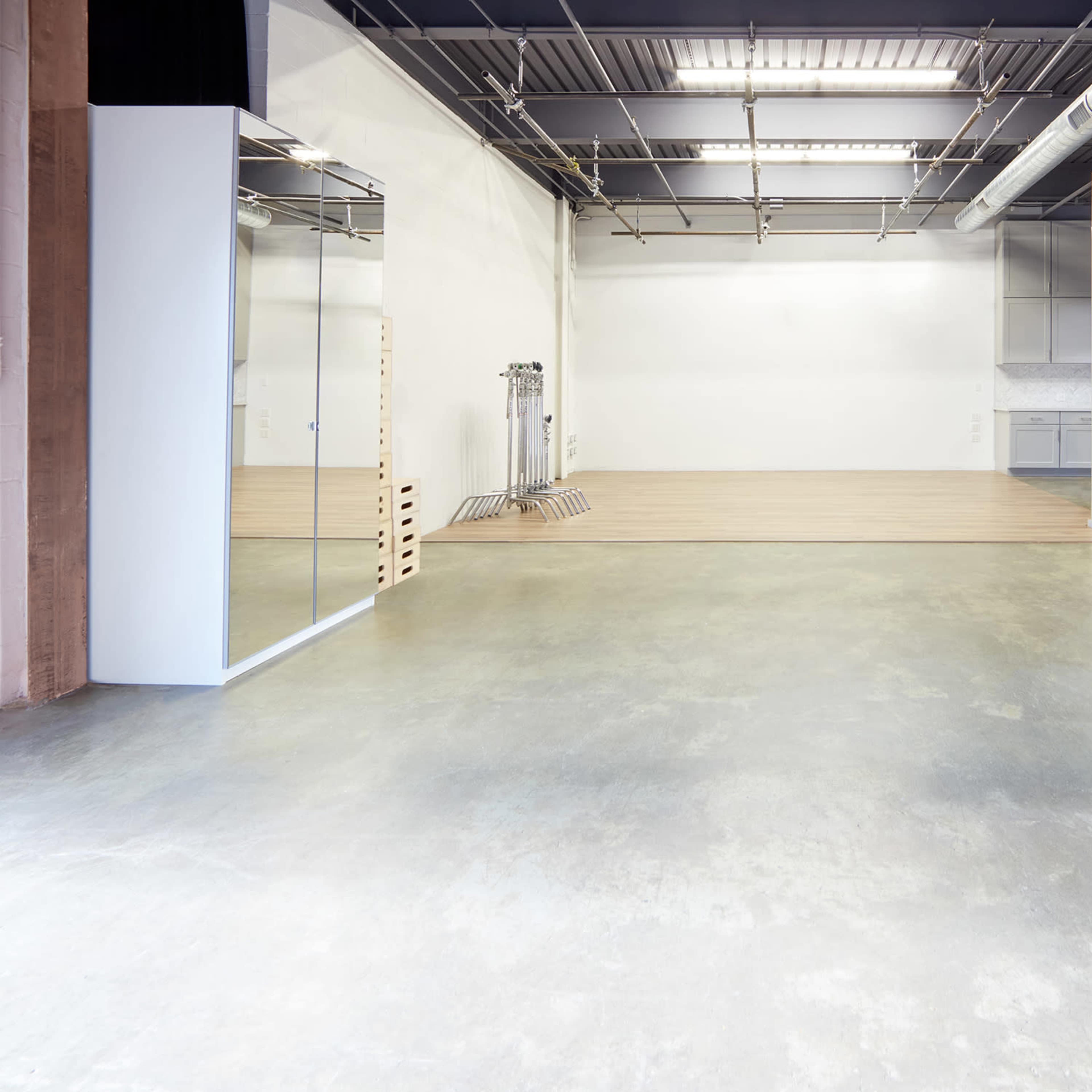 A spacious room with polished concrete floors, large mirrors on one side, and minimal furnishings, featuring an open layout and natural light.
