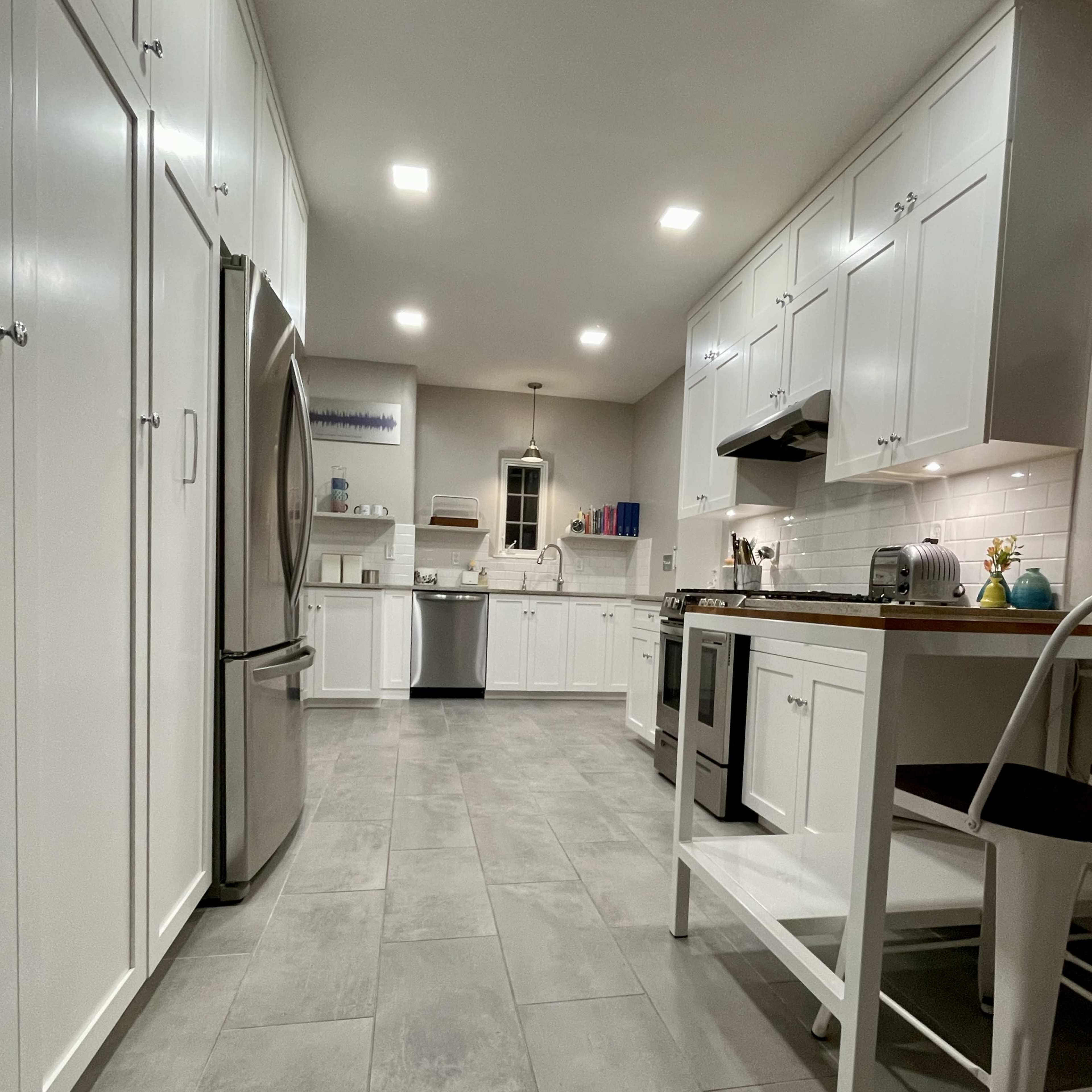 The kitchen features white cabinetry, stainless steel appliances, and a tile floor with a small dining area.