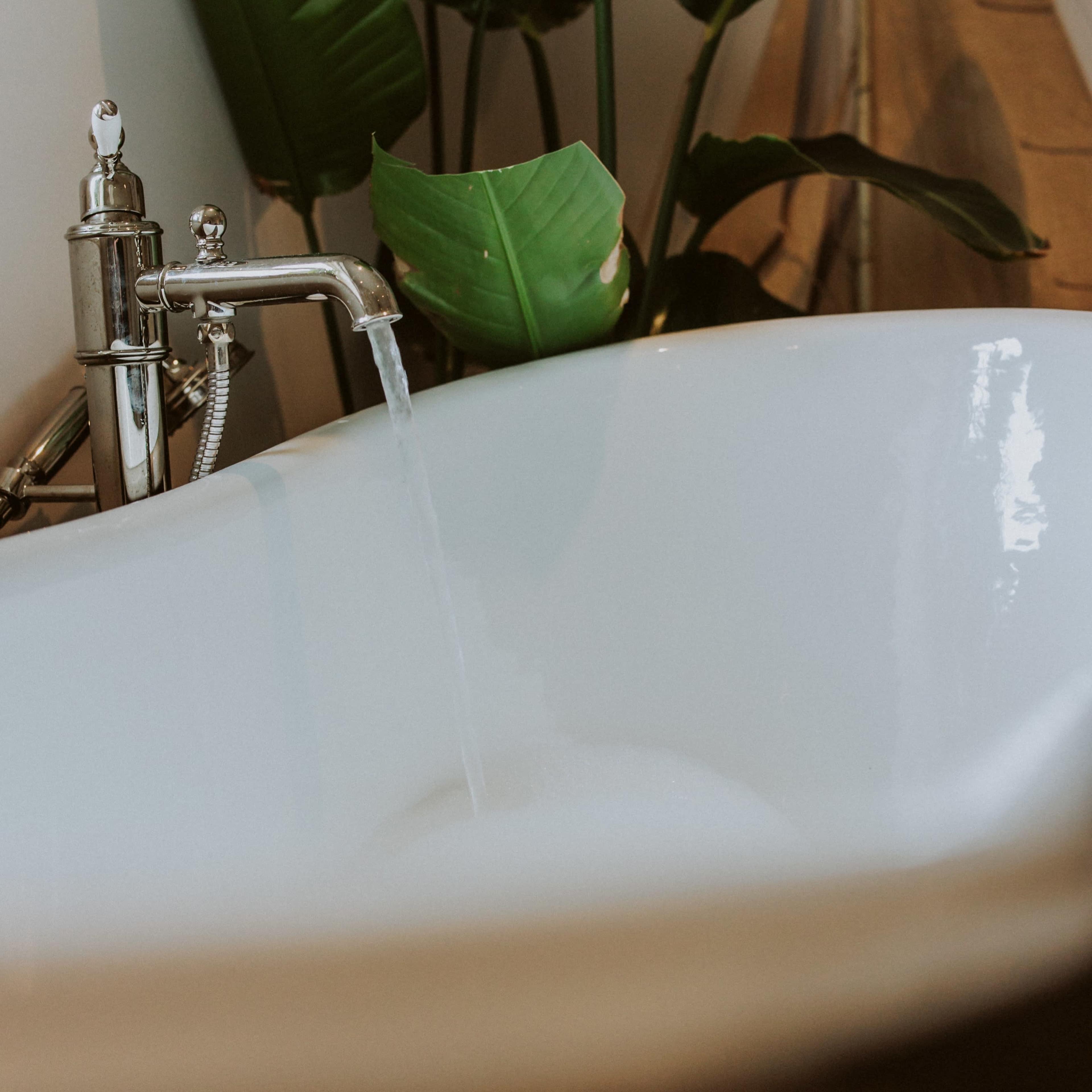 A modern bathtub with water flowing from a stylish faucet is positioned next to a potted plant.