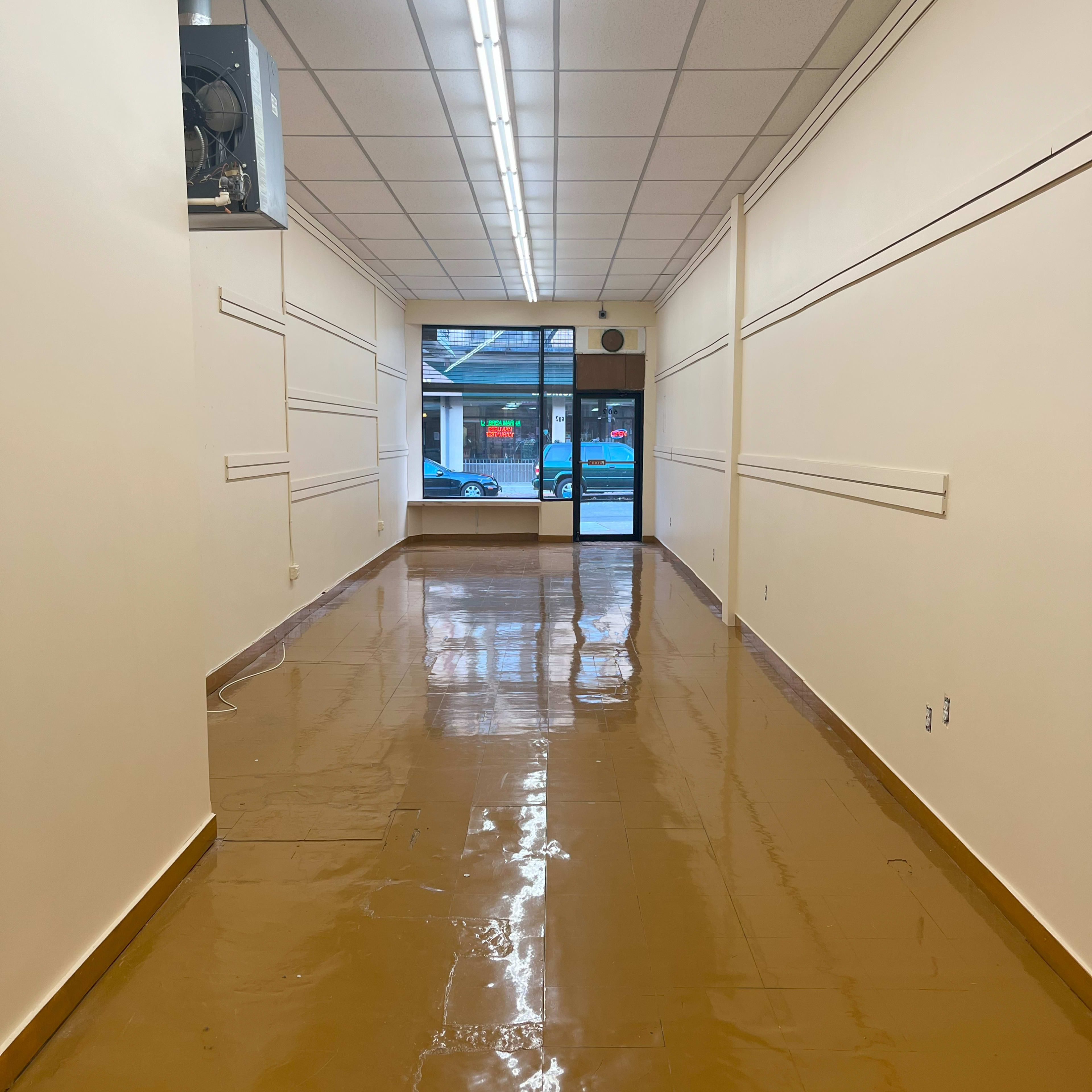 A long, empty hallway with a shiny brown floor and large windows at the far end.