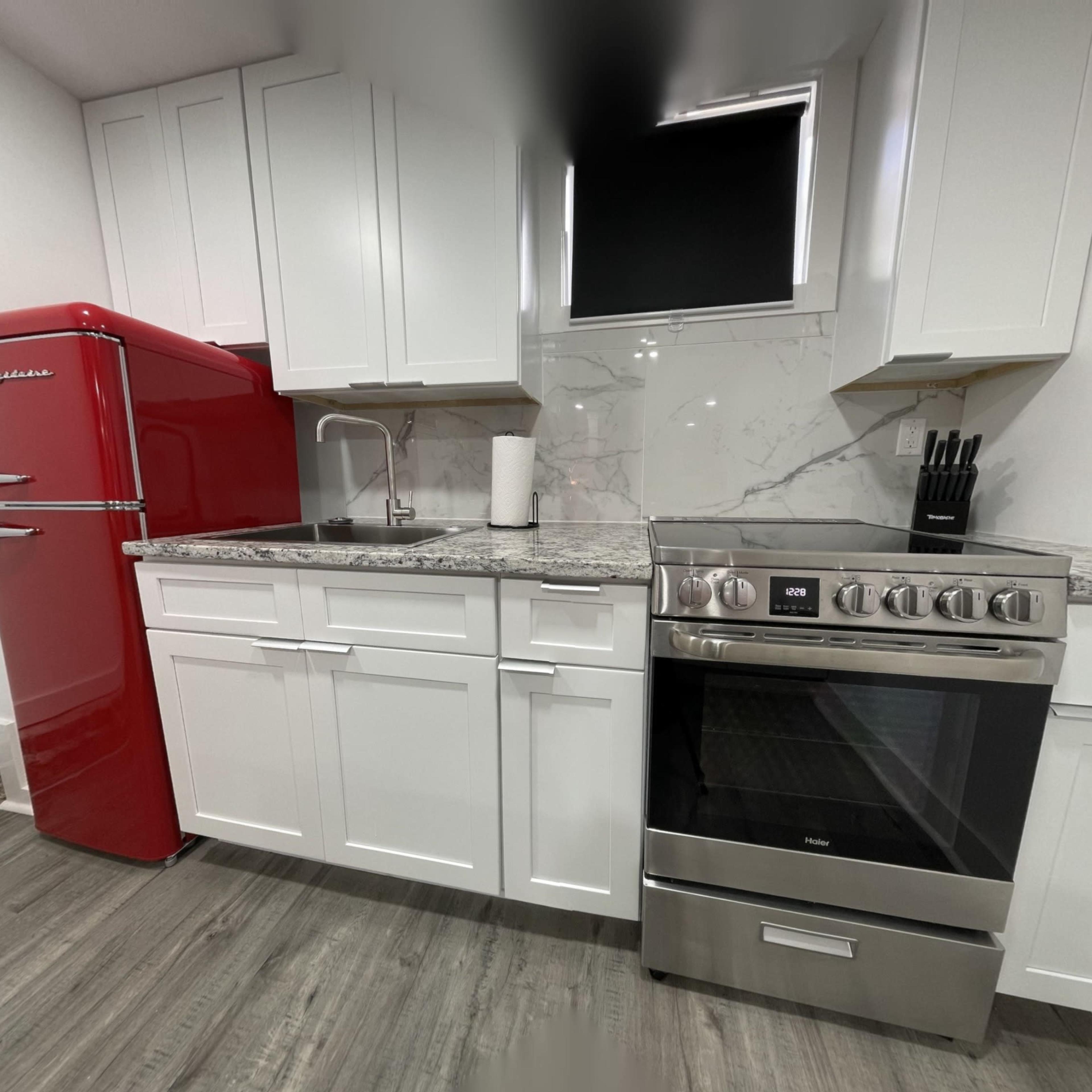 A modern kitchen featuring a red refrigerator, white cabinetry, and a stainless steel oven with a granite countertop.