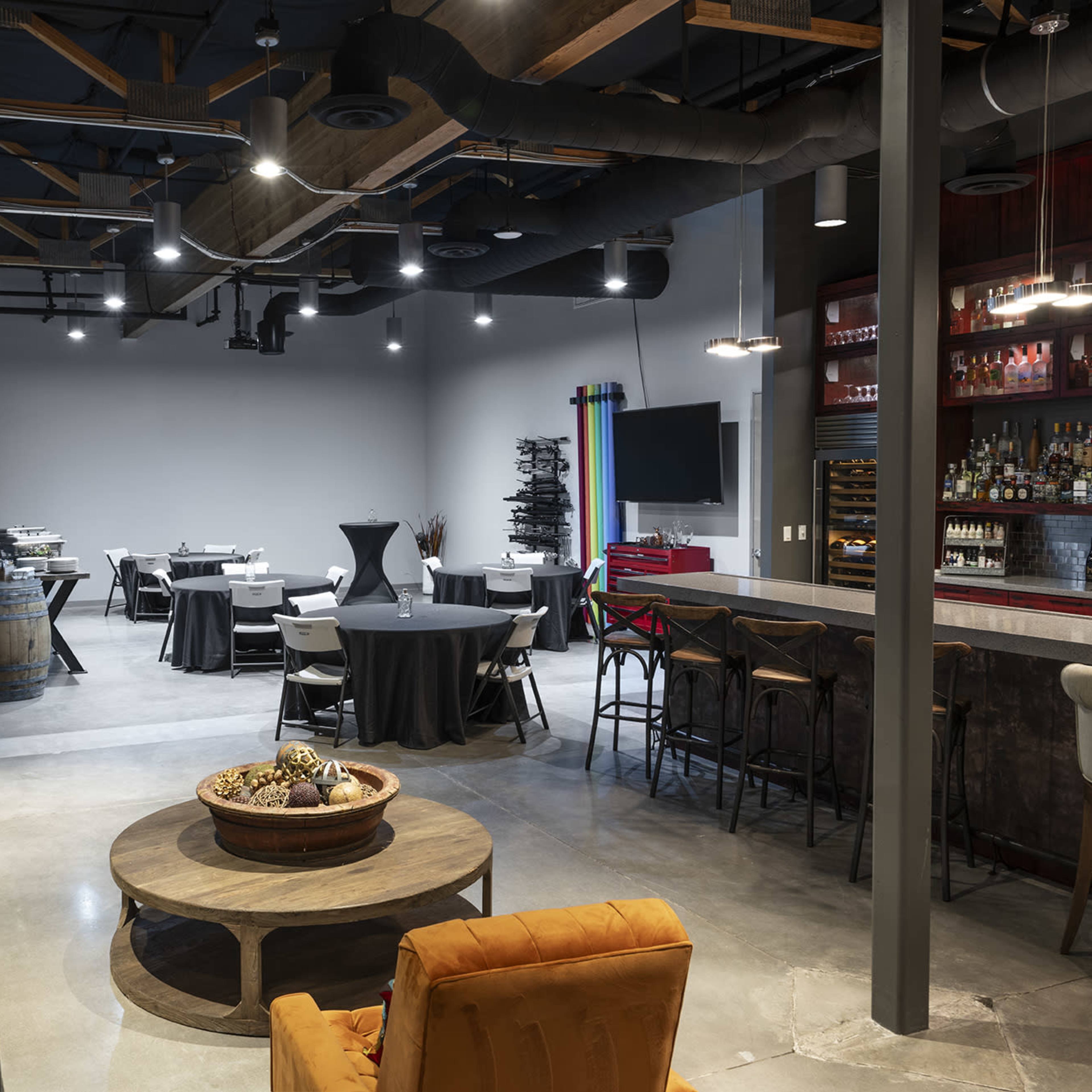 A modern interior of a restaurant or event space with a seating area featuring a sofa and decorative table, along with dining tables set up for an event in the background.