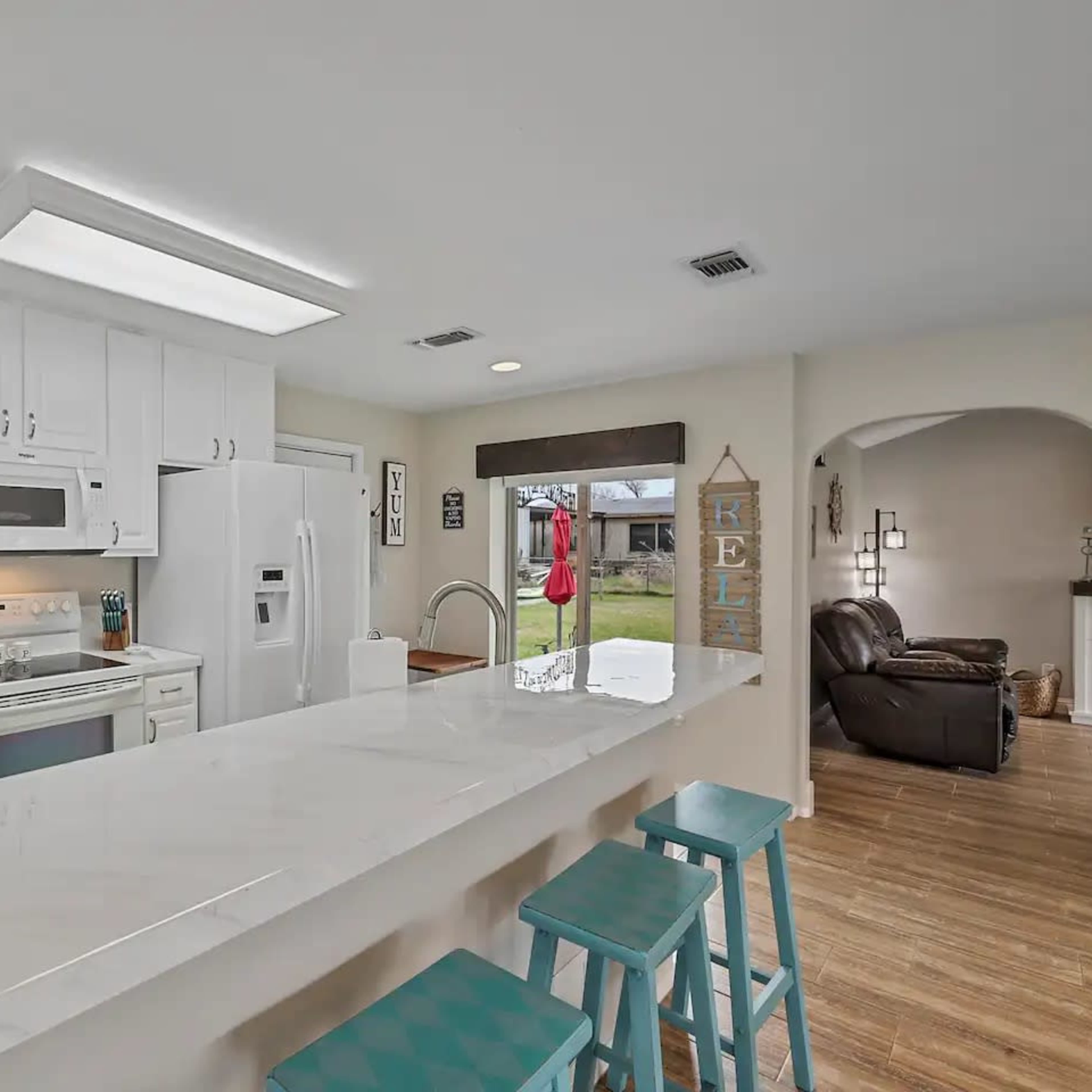 A modern kitchen features white cabinetry, stainless steel appliances, and a breakfast bar with turquoise stools.