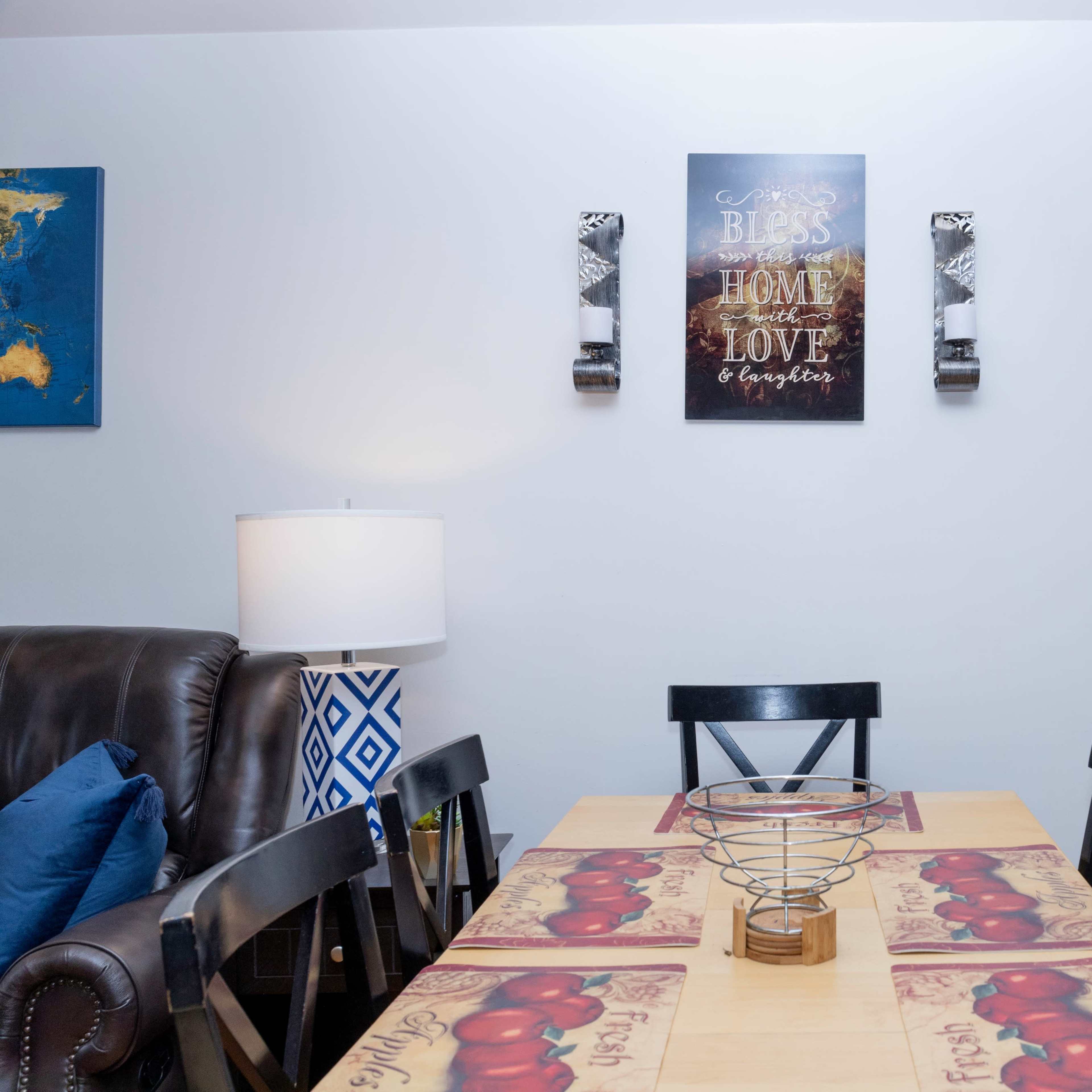 A dining area with a table set with a tablecloth featuring a fruit design, framed by a wall with decorative artwork and candles.