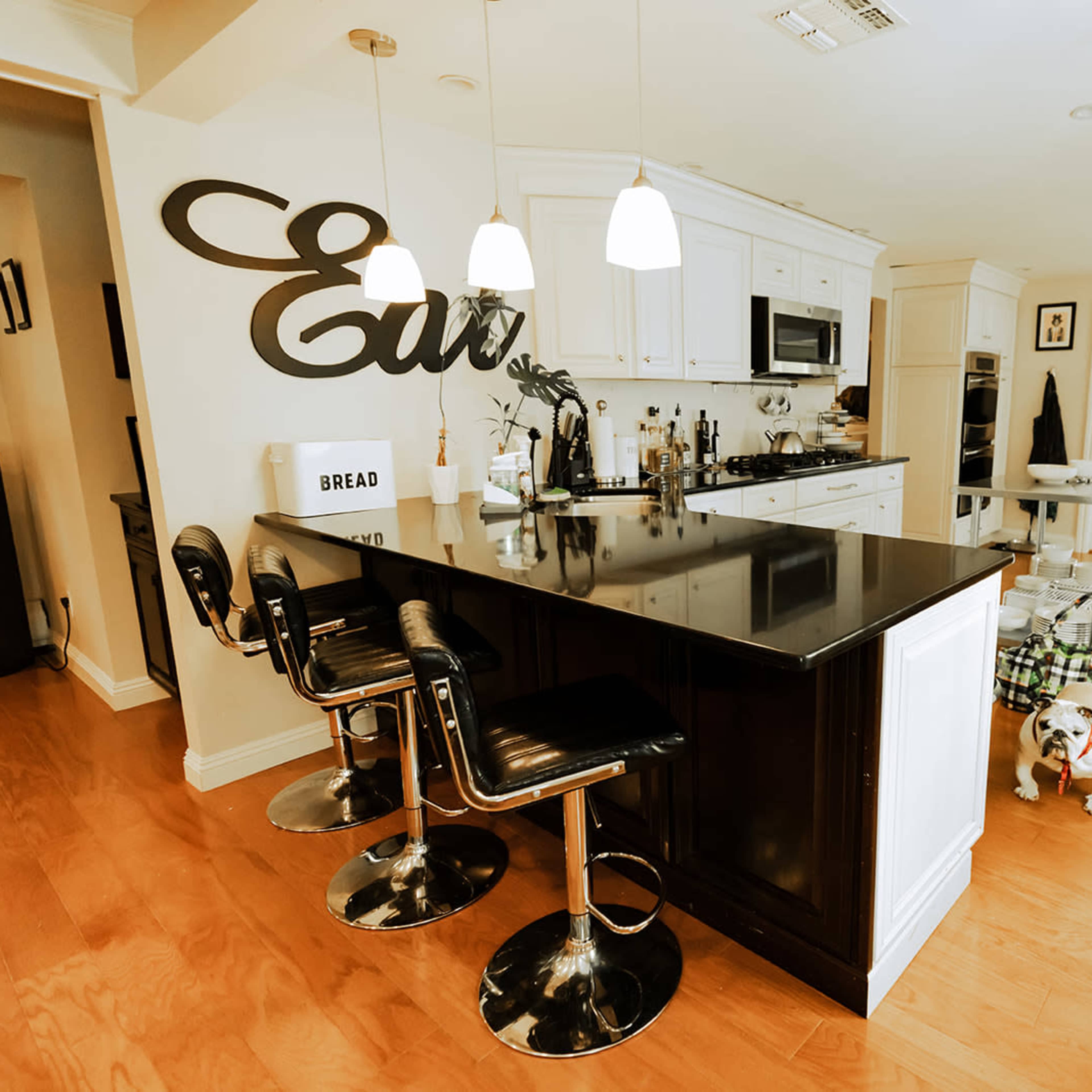 A modern kitchen with a black countertop island, bar stools, and a variety of appliances, alongside a dog lying on the floor.