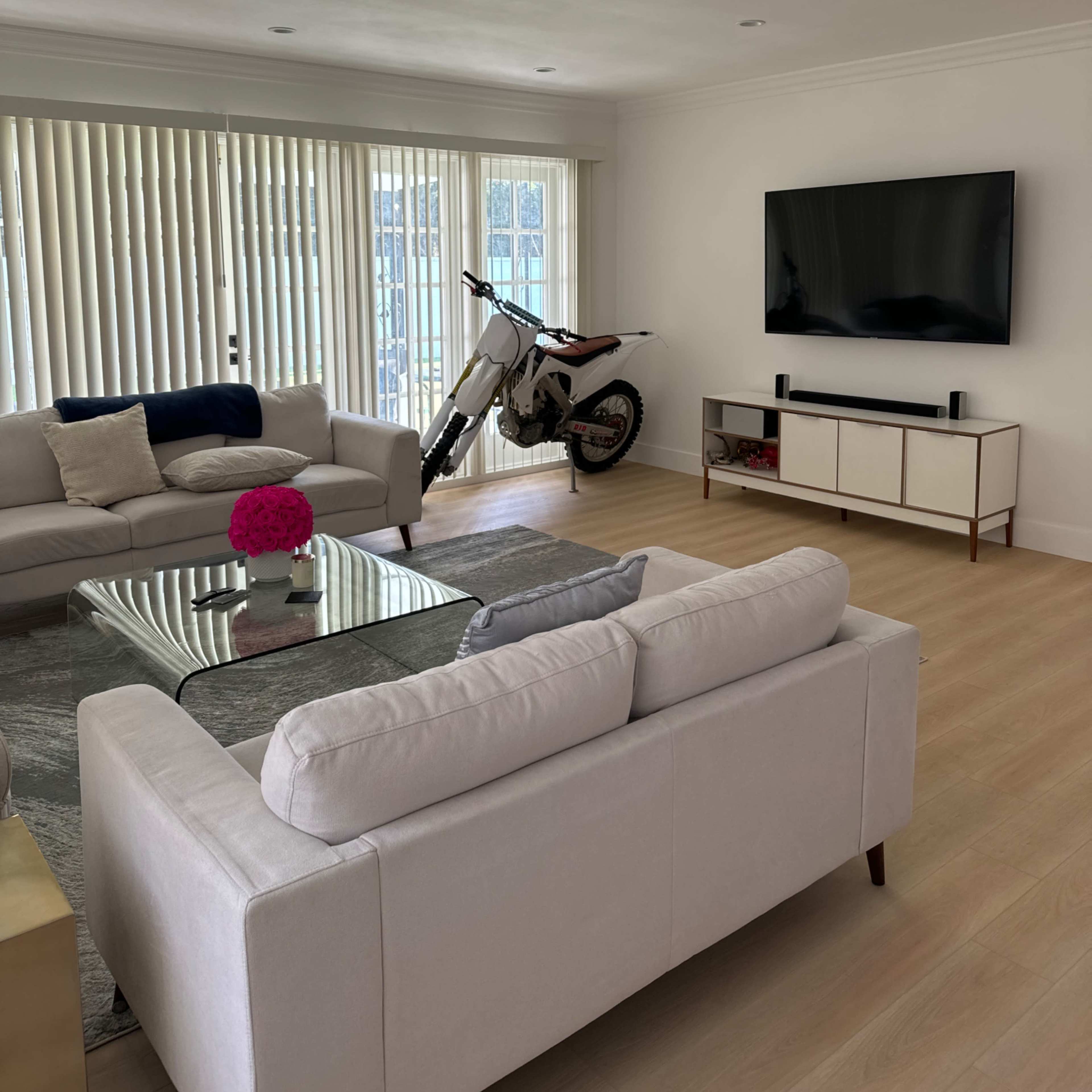 A modern living room features a dirt bike beside a couch and a television mounted on the wall.