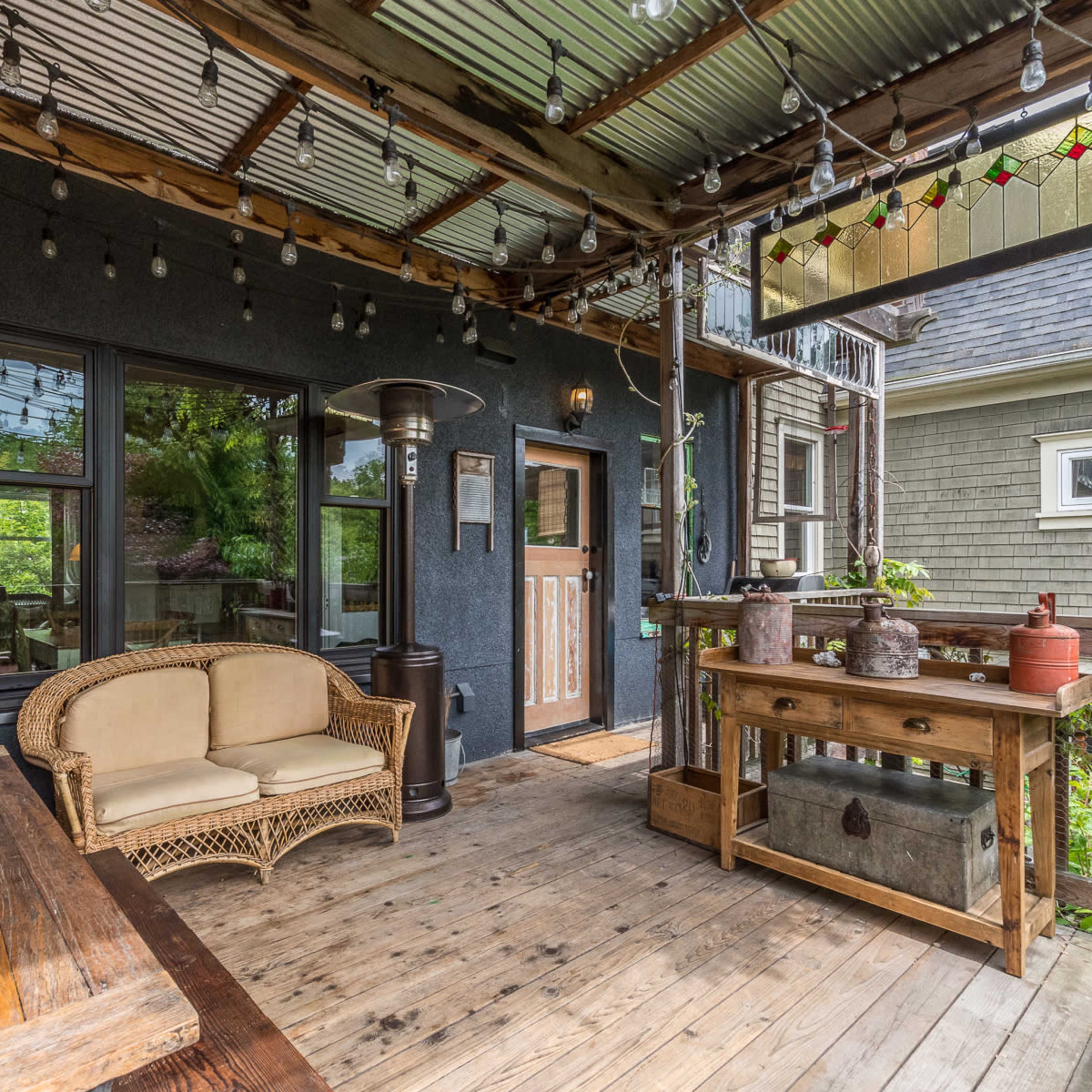 A covered outdoor deck with wooden flooring, a wicker sofa, and decorative hanging lights.