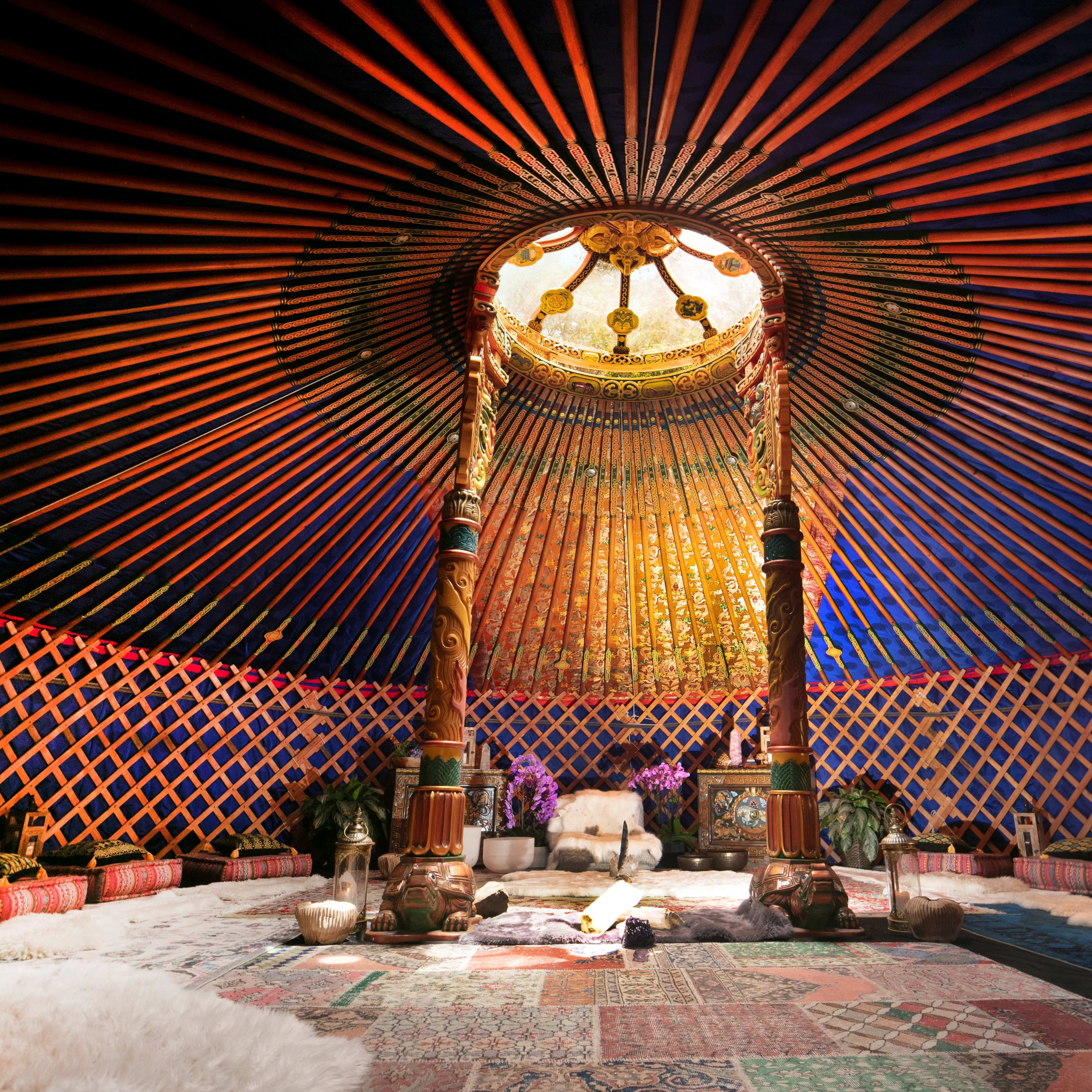 The interior of a yurt features a circular skylight, wooden pillars, and decorative walls adorned with vibrant patterns.