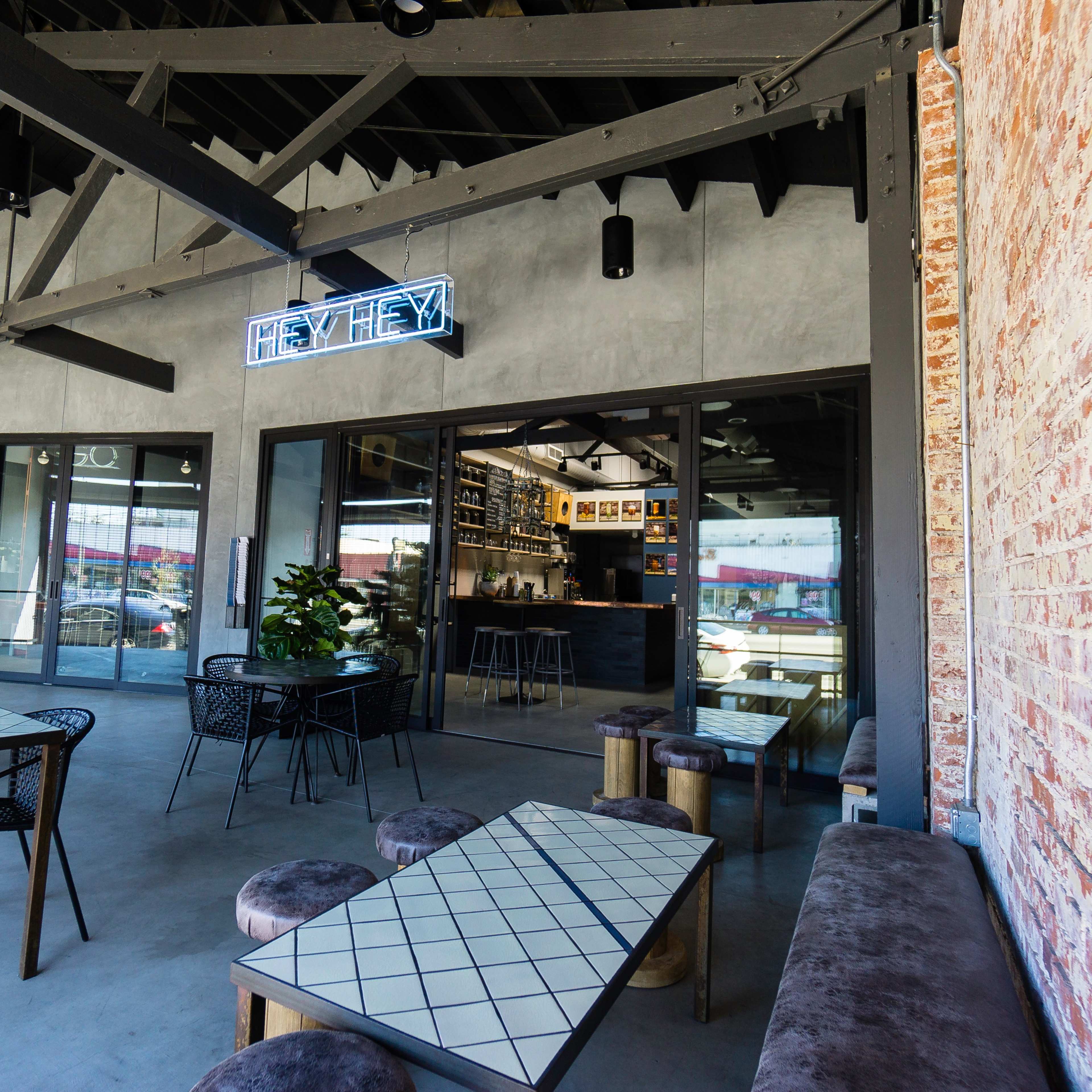 A modern café with a brick wall, large windows, and sleek furniture, featuring indoor plants and a bar area in the background.