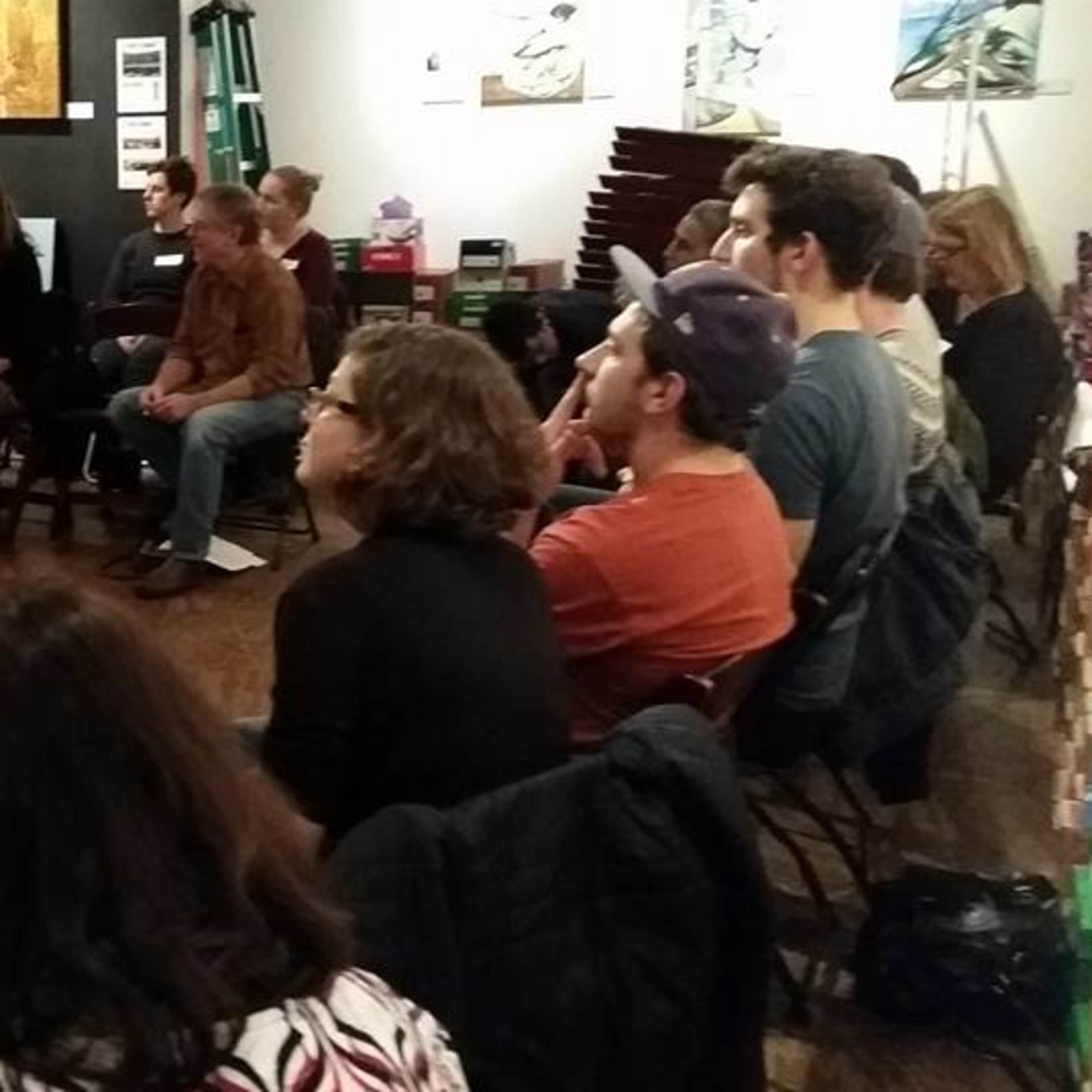 A large group of people is seated in a circle in an art gallery, engaging in discussion while facing each other.
