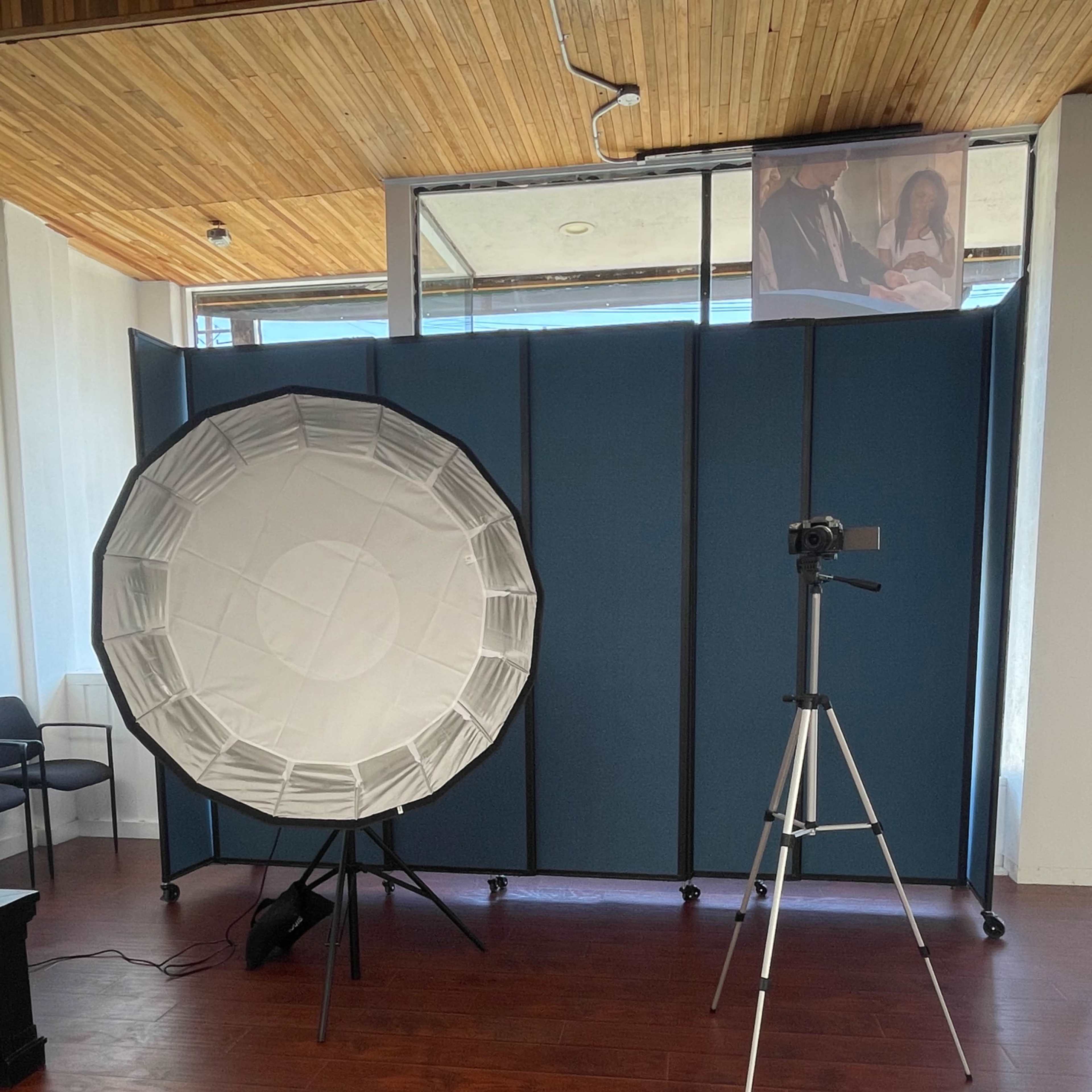 A photography setup with a large softbox and a camera mounted on a tripod, positioned in front of a blue divider.