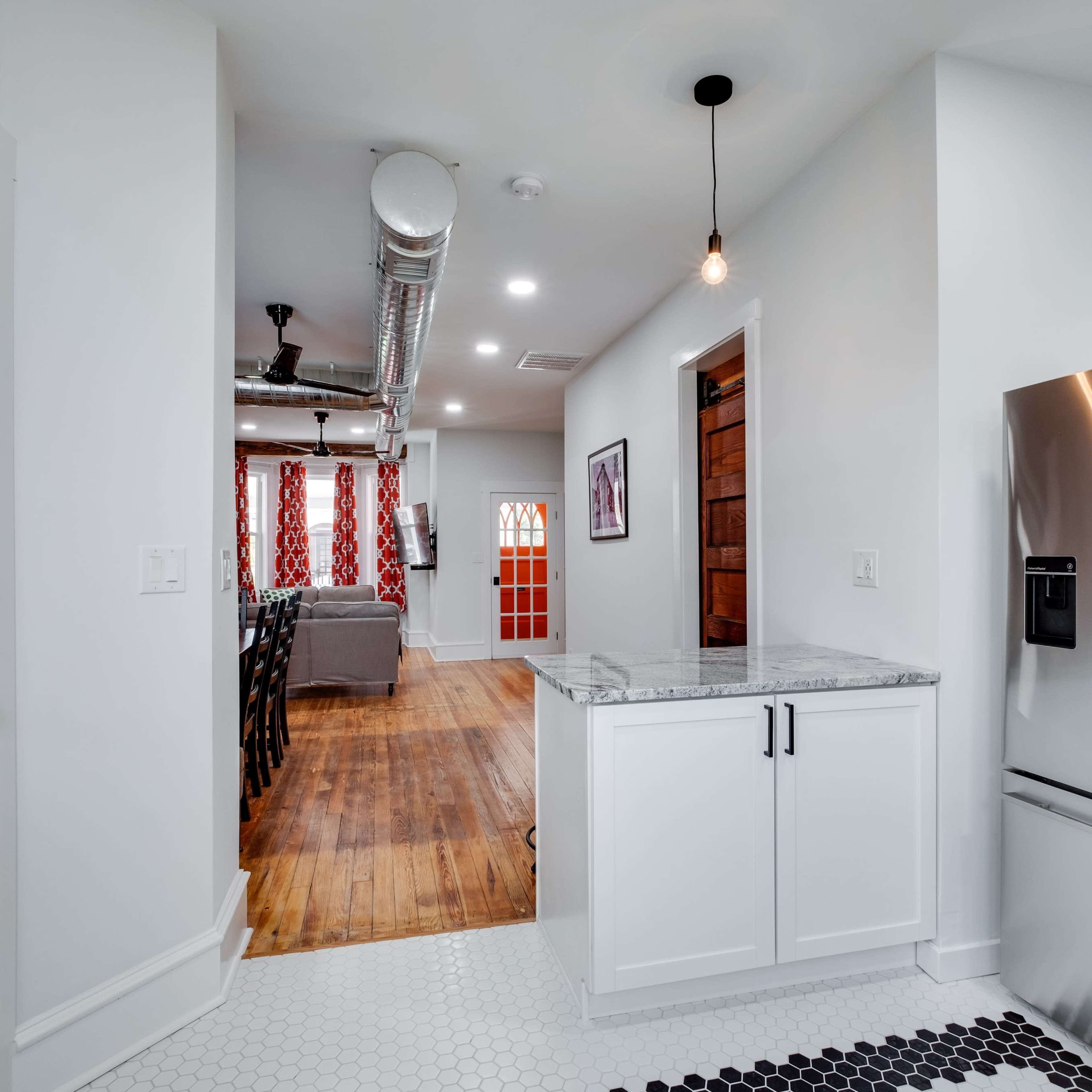 A modern kitchen features a stainless steel refrigerator, white cabinets, and a view into a living area with a cozy seating arrangement.