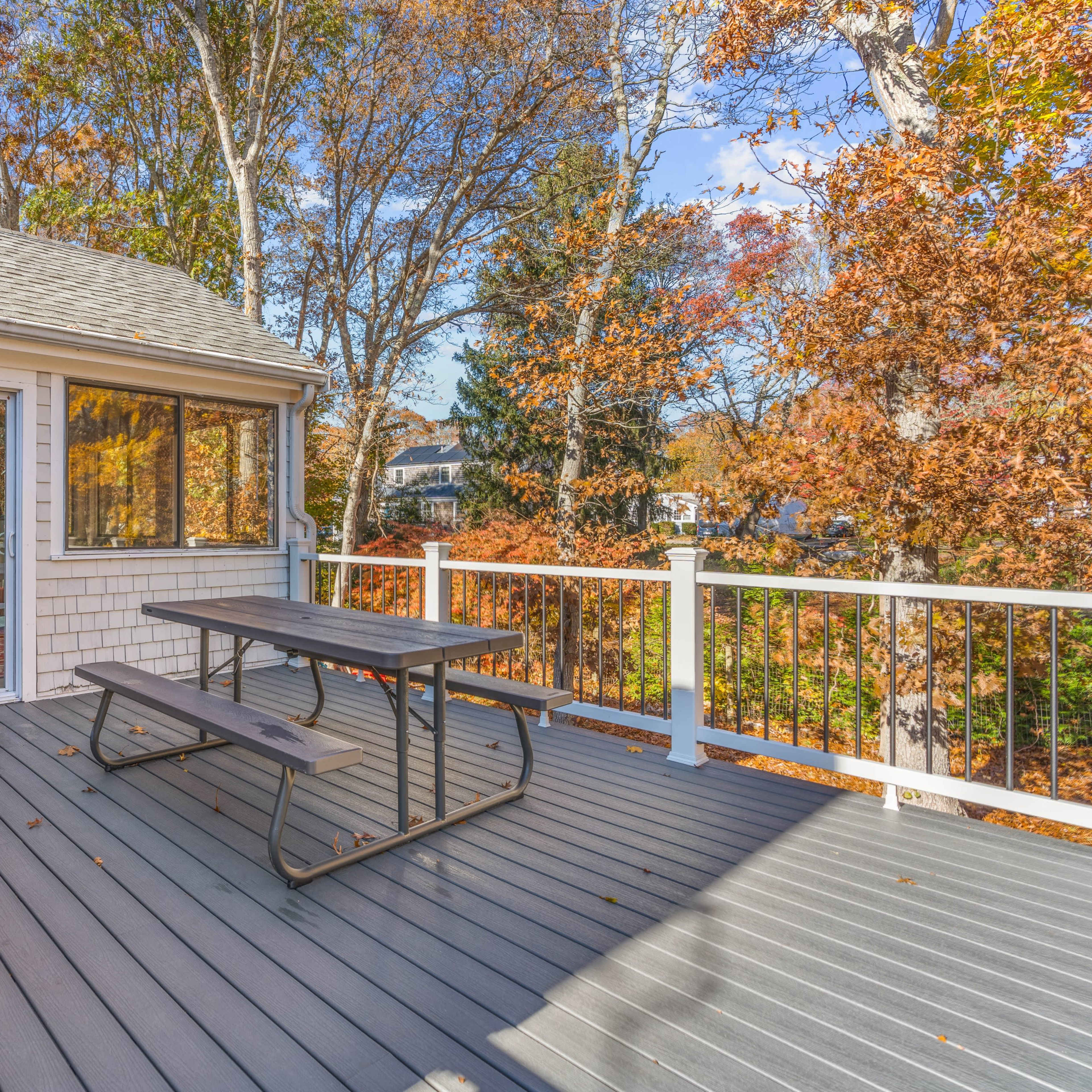 A wooden deck features a picnic table and a grill, surrounded by trees with autumn foliage.