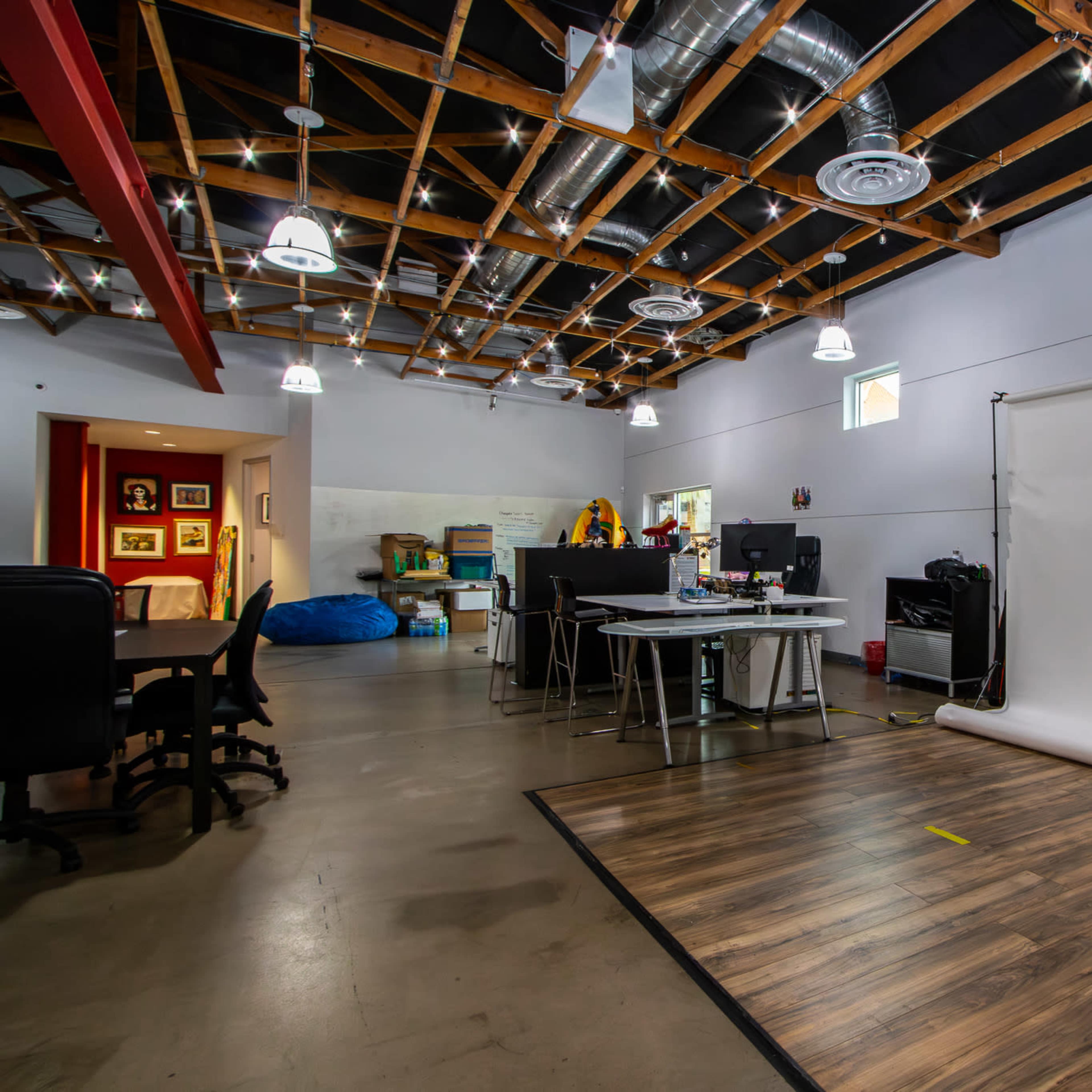 A spacious studio with a wooden floor, a photography backdrop, and several workstations set up along the left side.