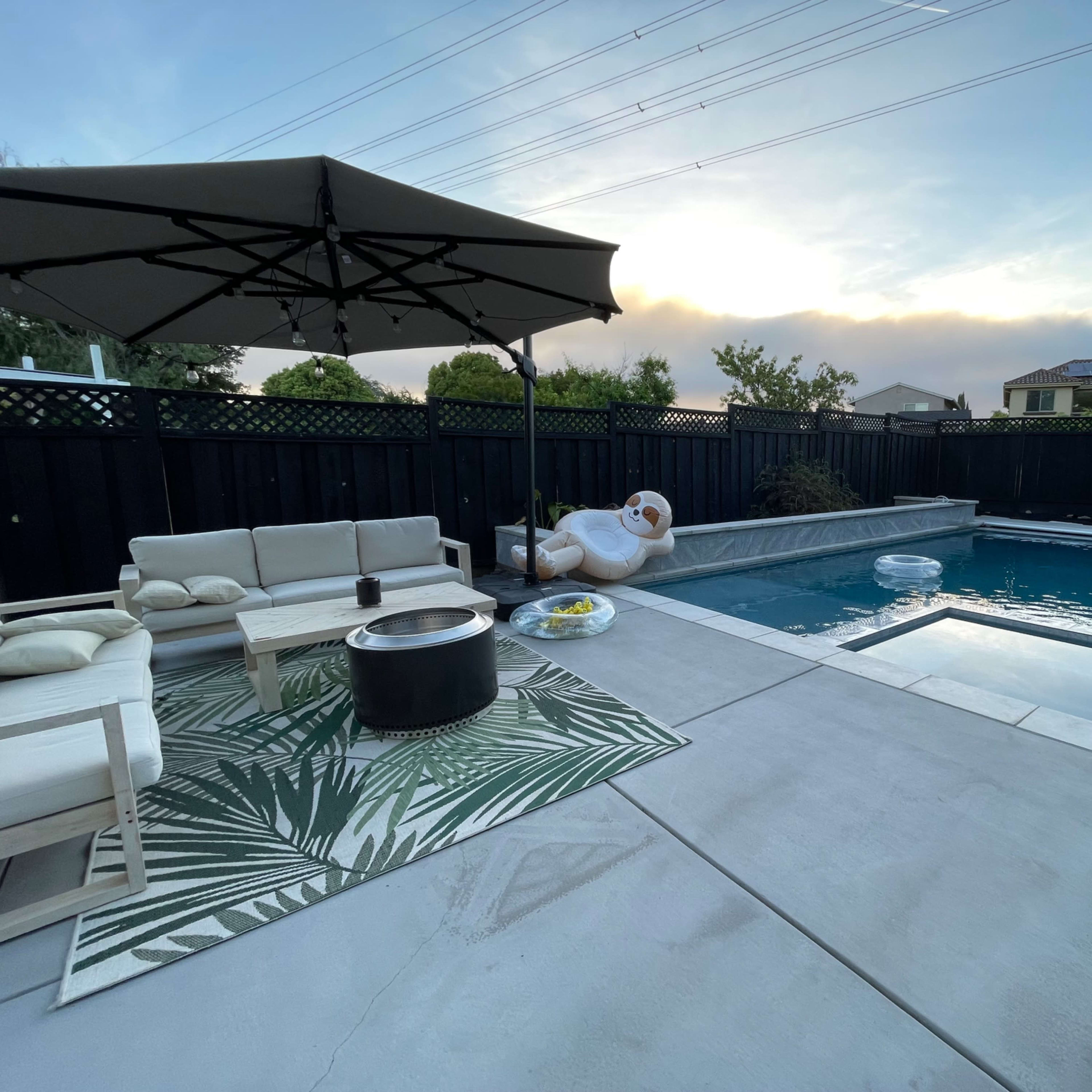 A modern backyard with a swimming pool, patio seating under an umbrella, and a floating inflatable in the water.