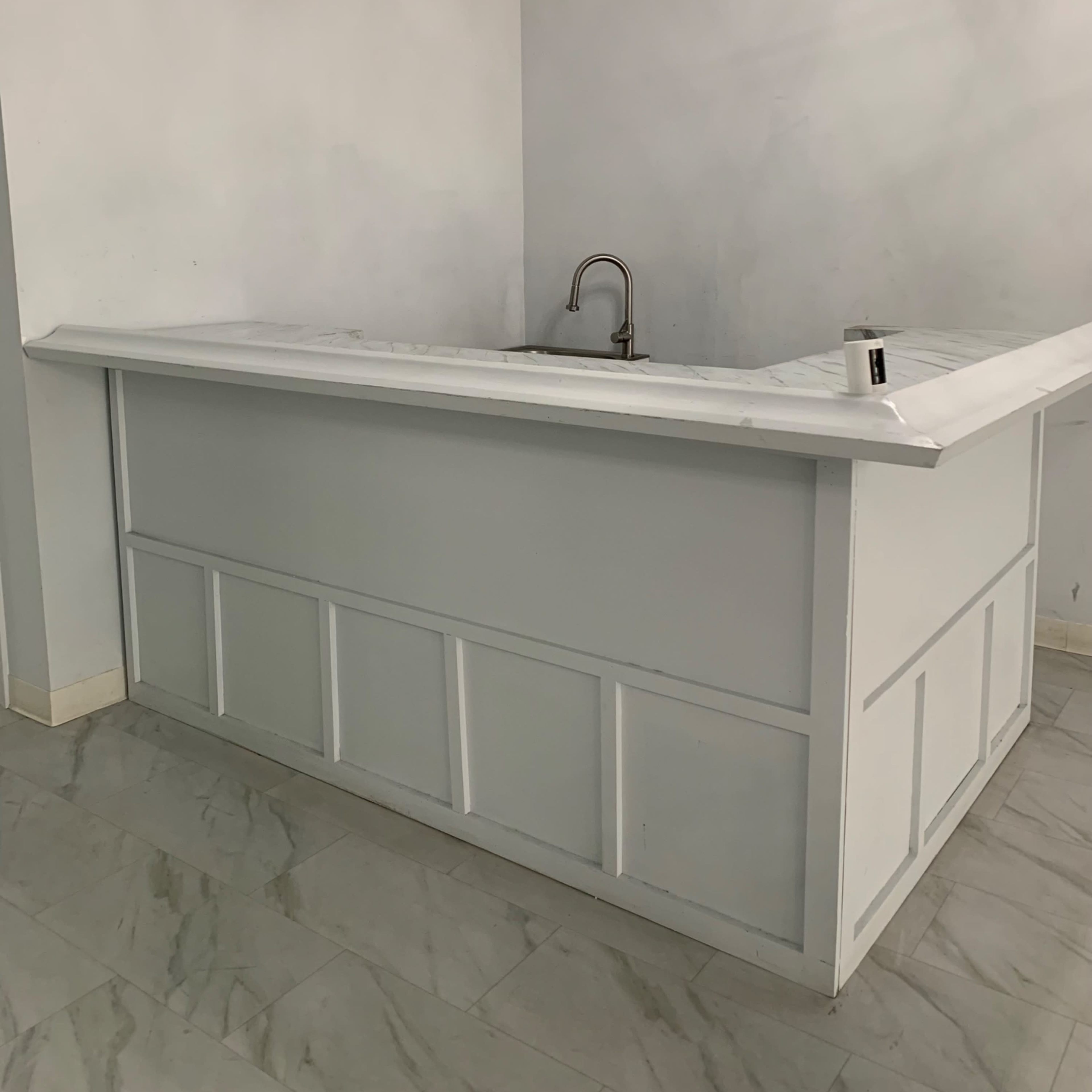 A white kitchen counter with a sink, set against a light-colored wall in a tile-floored room.