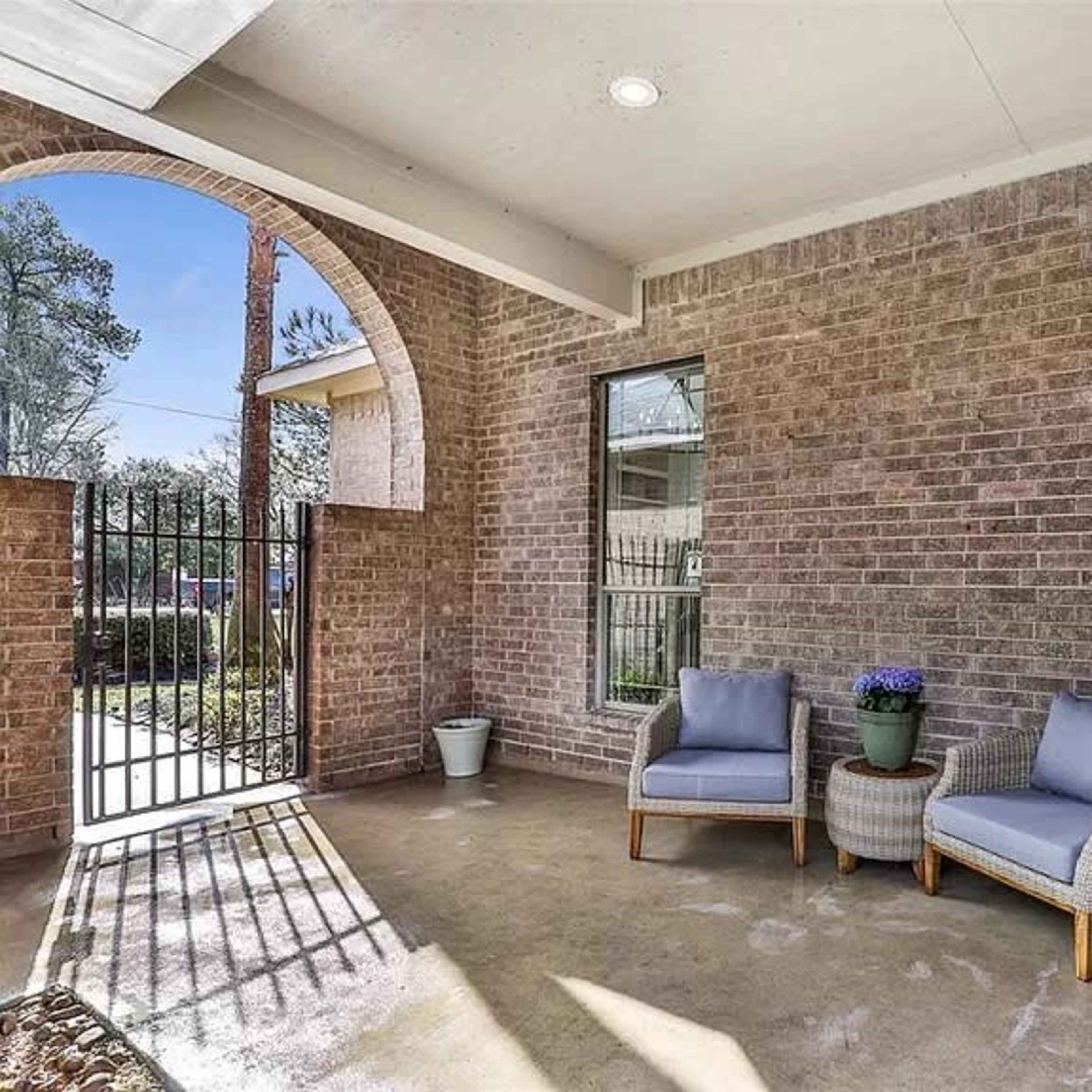 A covered porch area featuring two blue chairs, a potted plant, and a gated entrance.