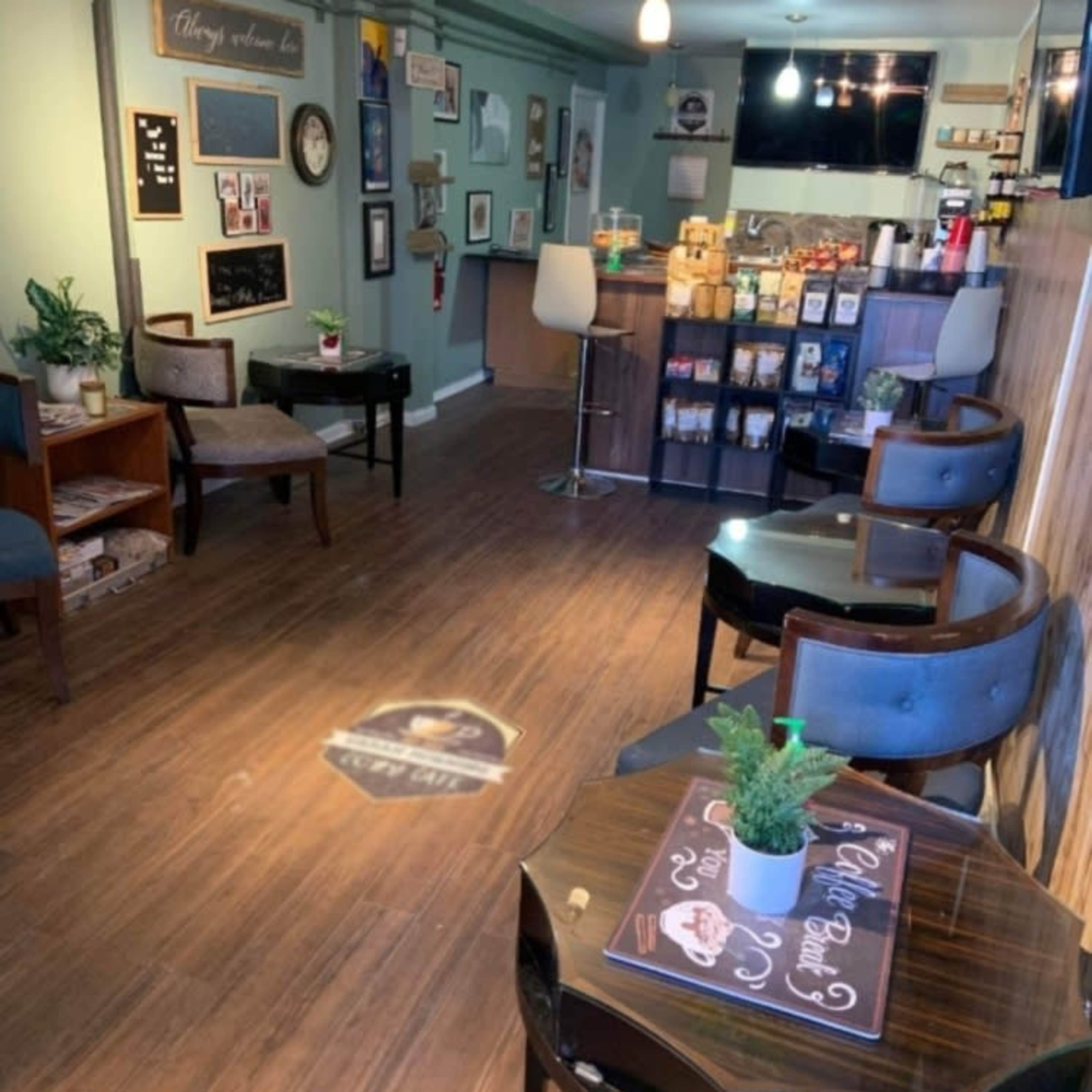 A cozy café interior with wooden floors, a counter displaying various products, and seating arranged around dark tables.