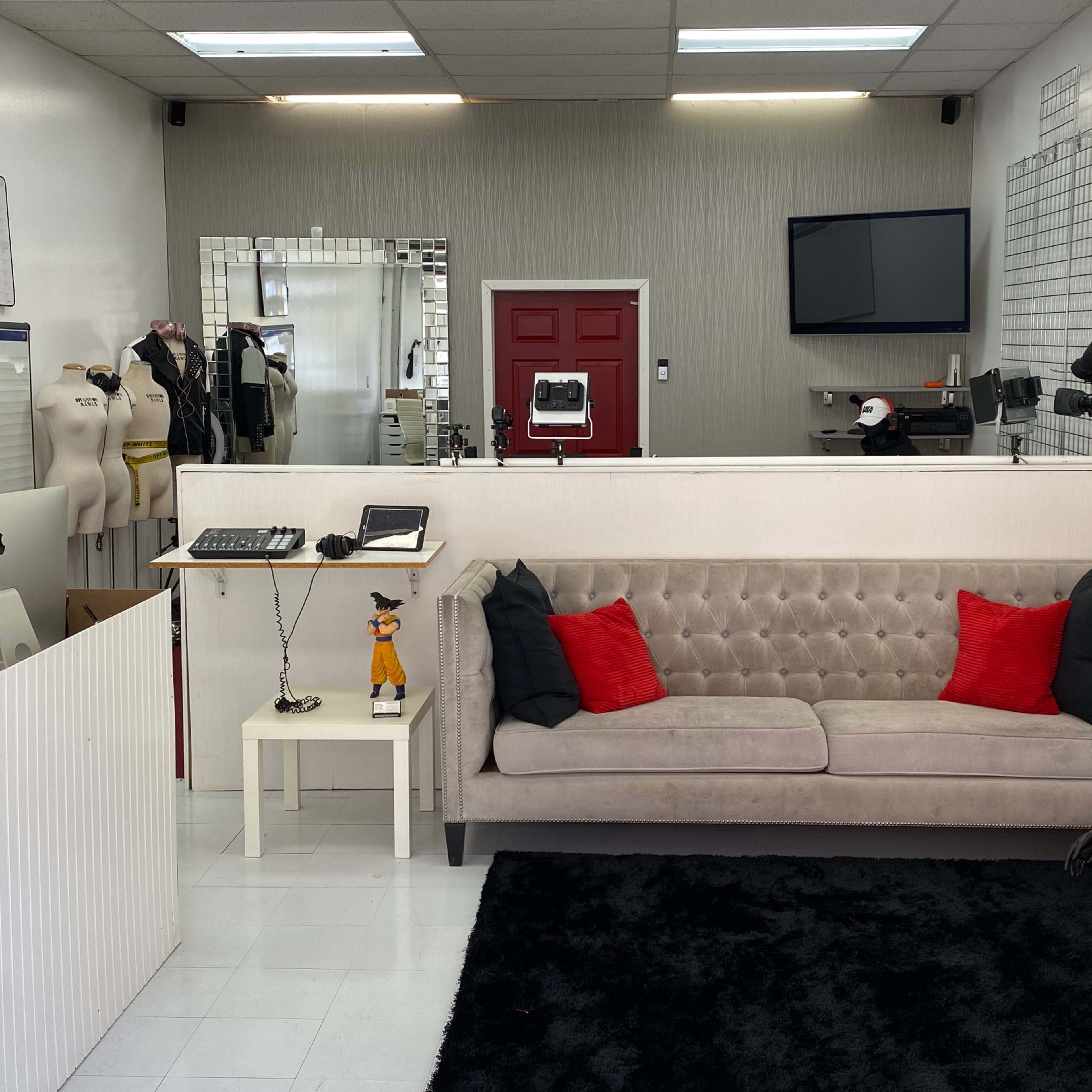 A modern boutique interior featuring a gray sofa with red pillows, a reception area with a computer, and several mannequins dressed in clothing.
