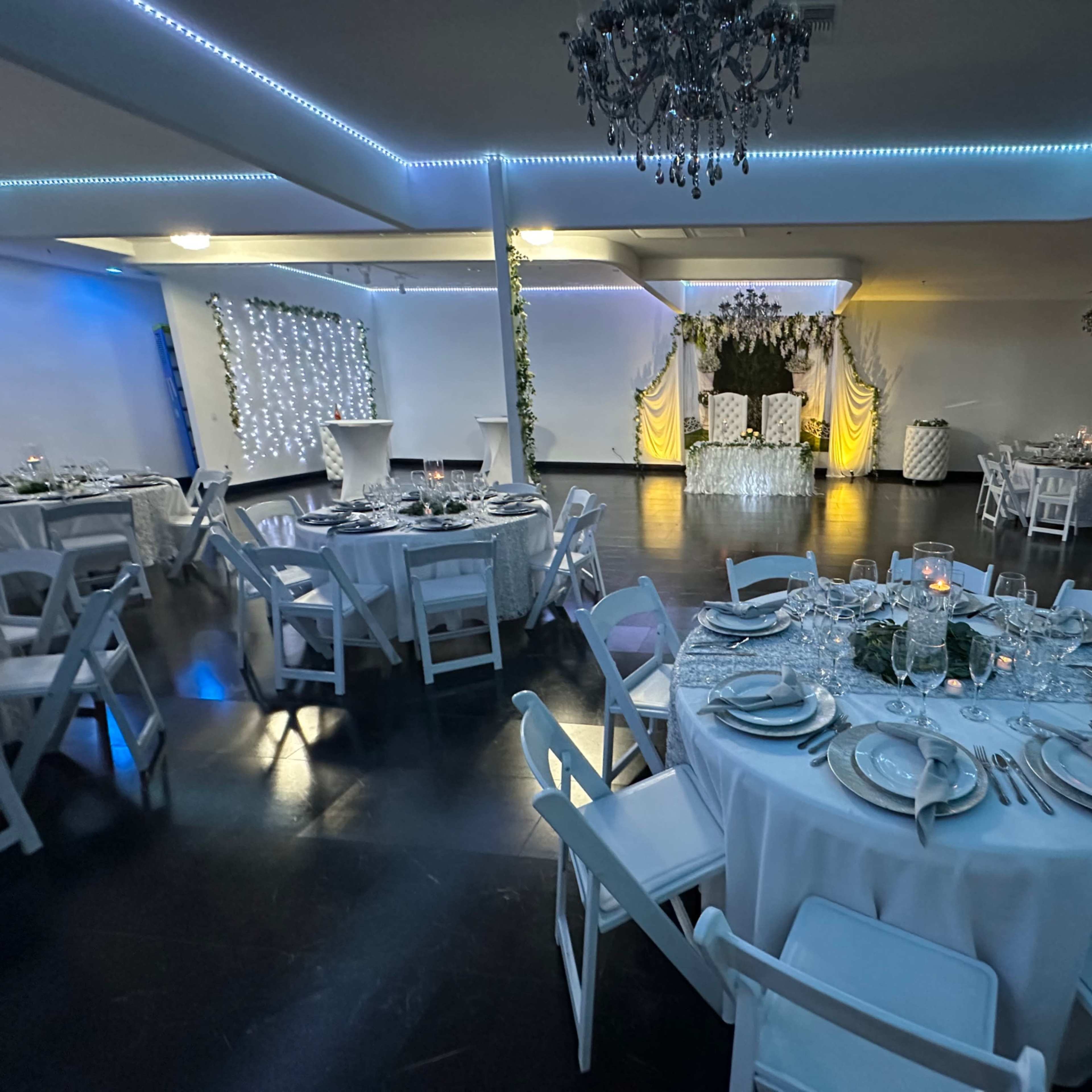A banquet hall set for an event, featuring elegantly arranged tables with dinnerware and a decorated stage at the front.