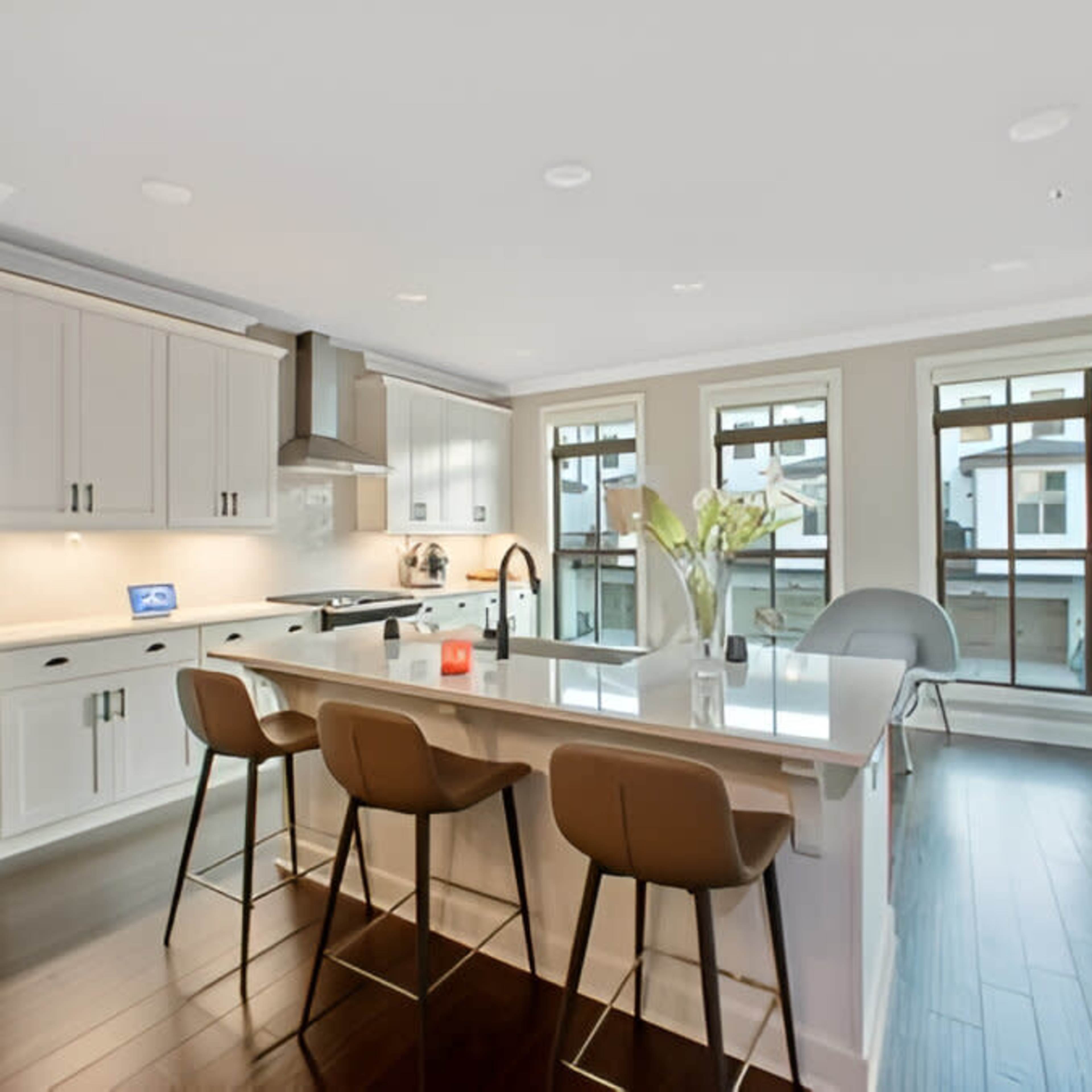 A modern kitchen with a white cabinetry, an island with seating, and large windows providing natural light.