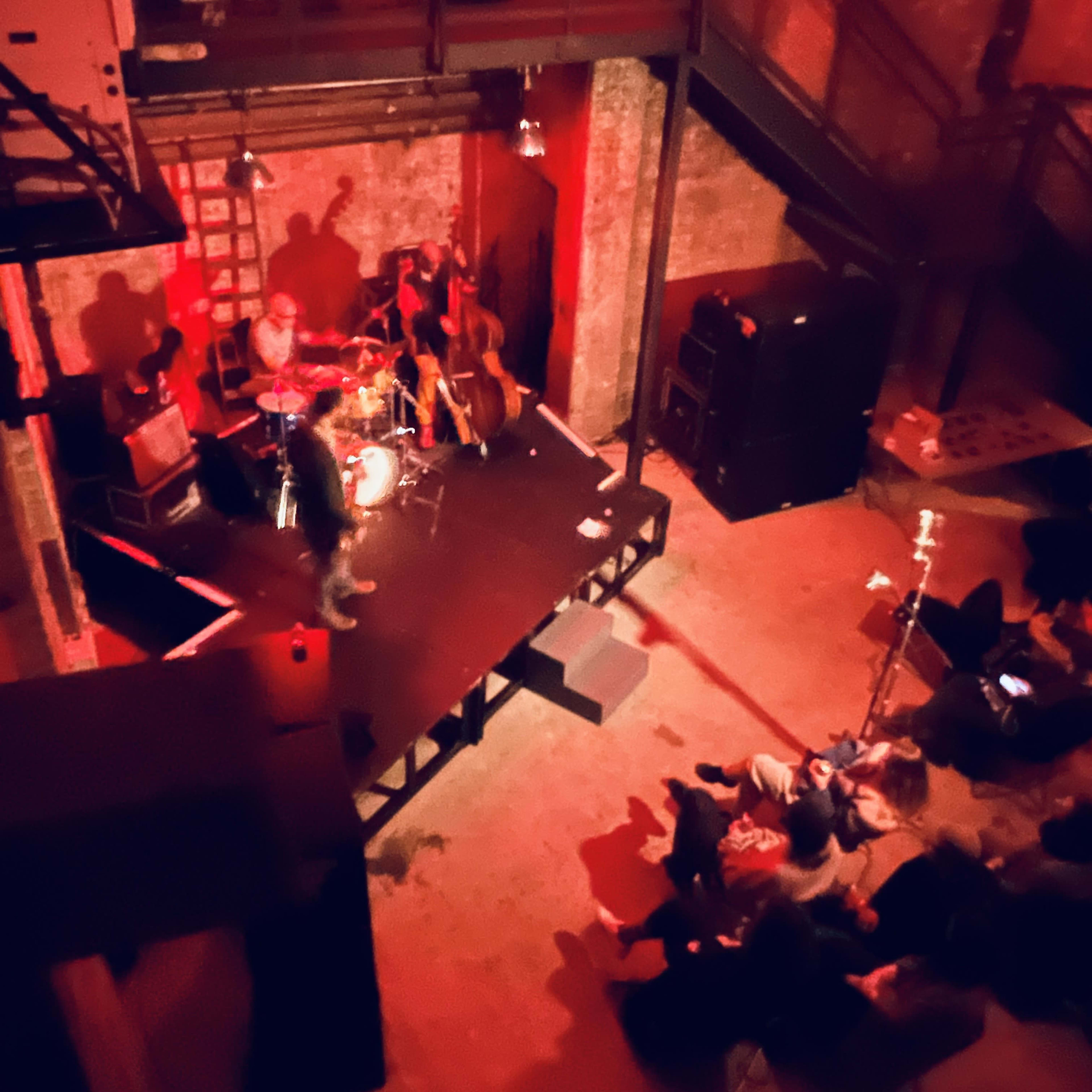 A musician performs on stage in a dimly lit venue while an audience sits in front of the stage.