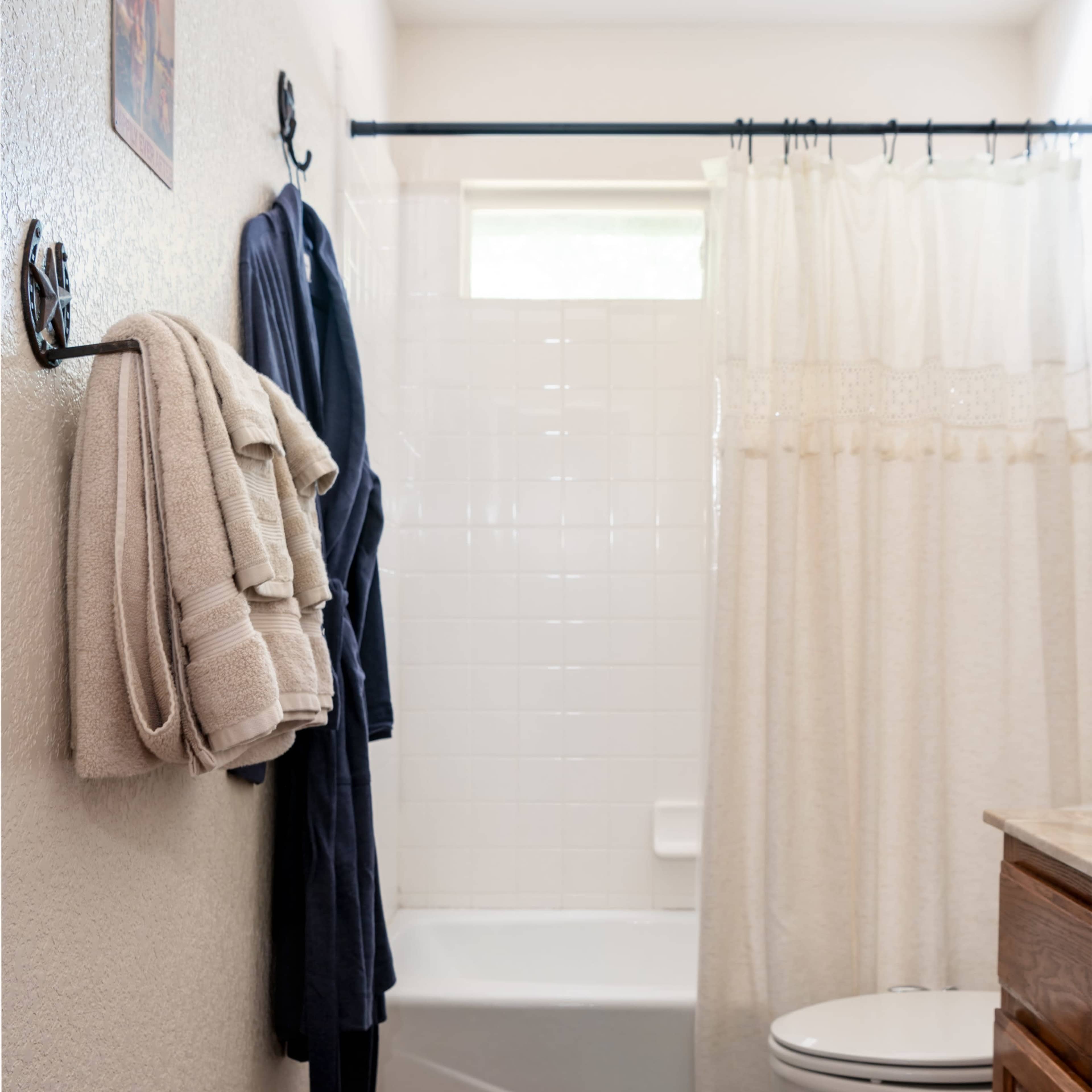 A bathroom with a bathtub, shower curtain, toilet, and neatly hung towels and a robe on a rack.