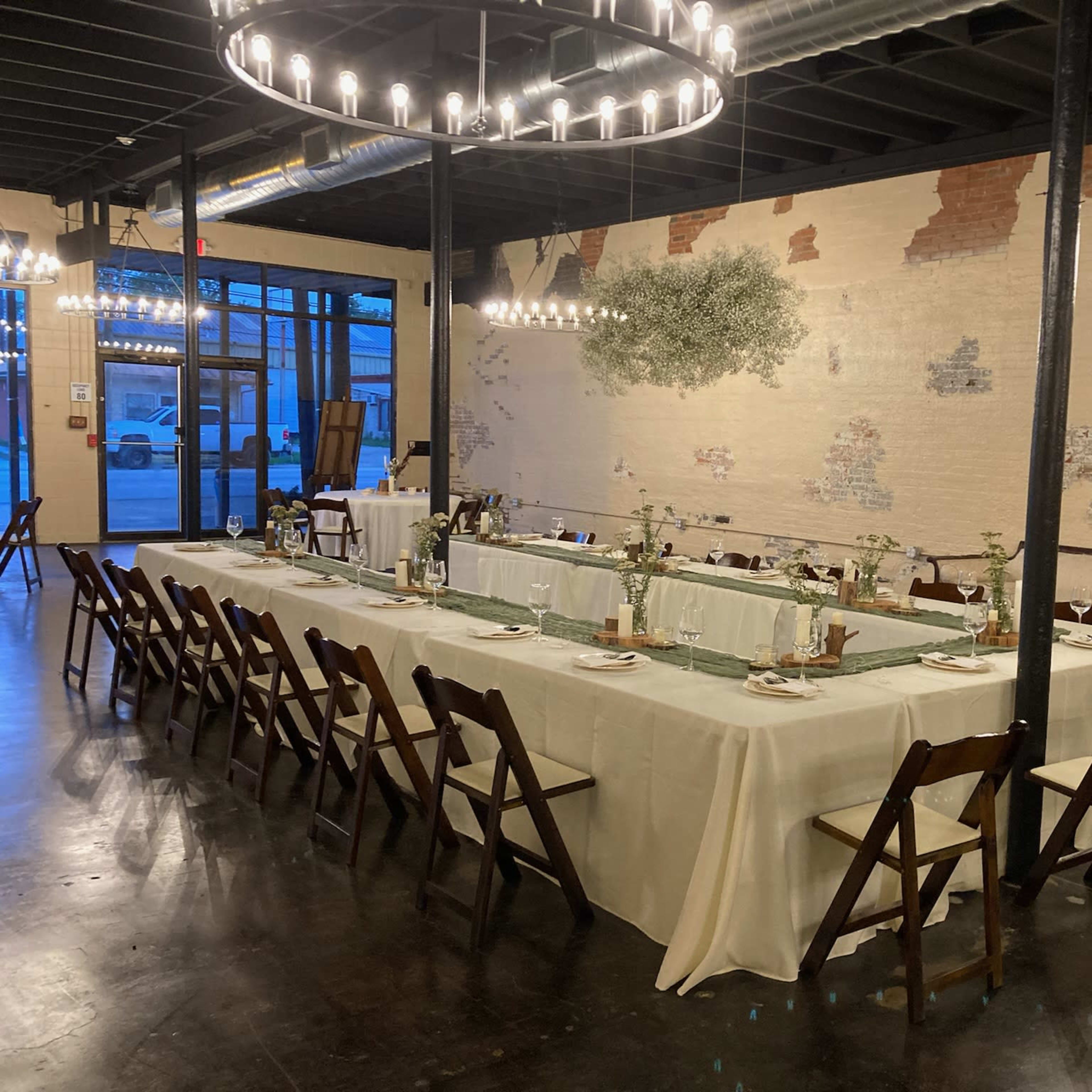 A long dining table is set for a meal in a venue with exposed brick walls and modern lighting fixtures.