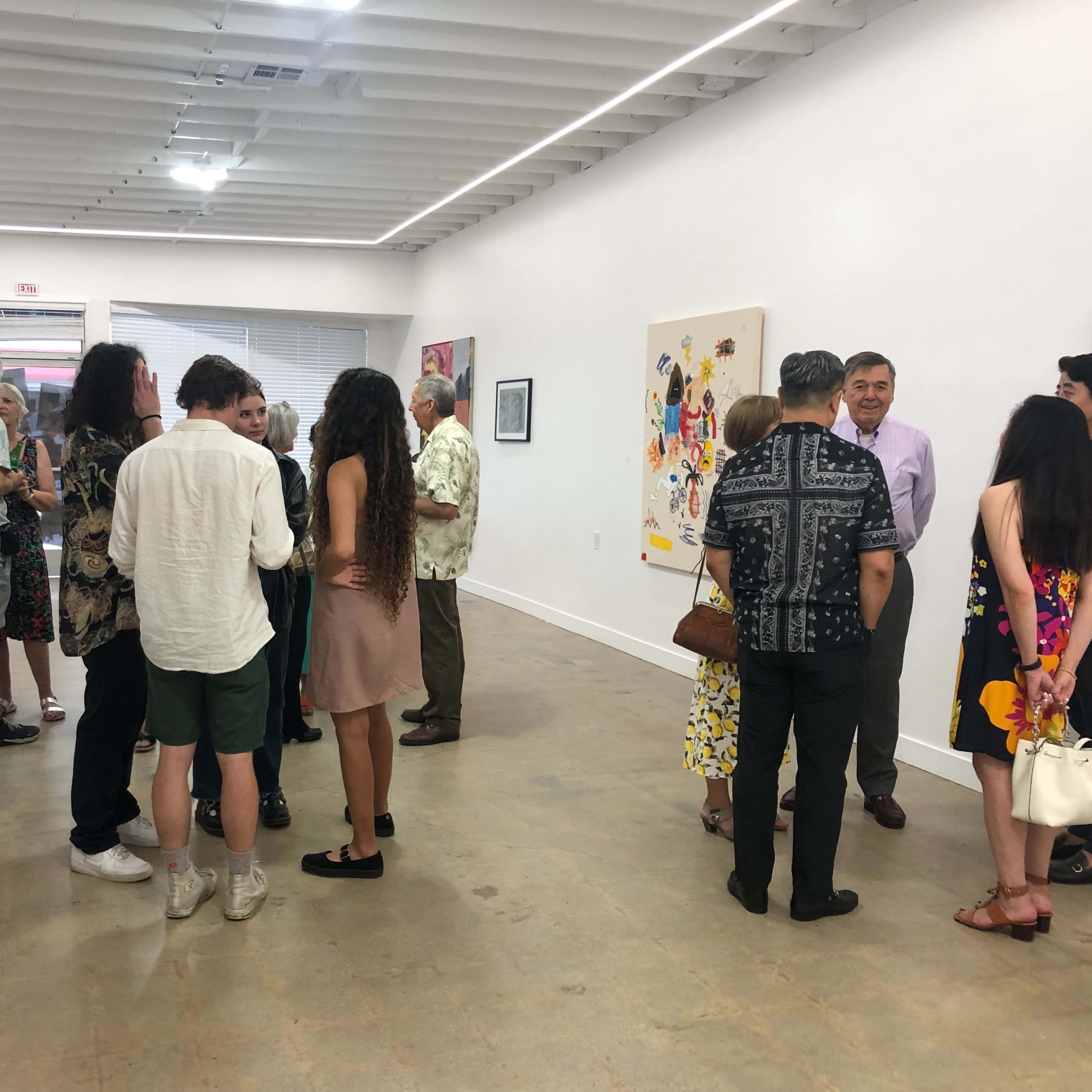 A group of diverse individuals gathers in an art gallery, engaging in conversation while observing various artworks displayed on the walls.