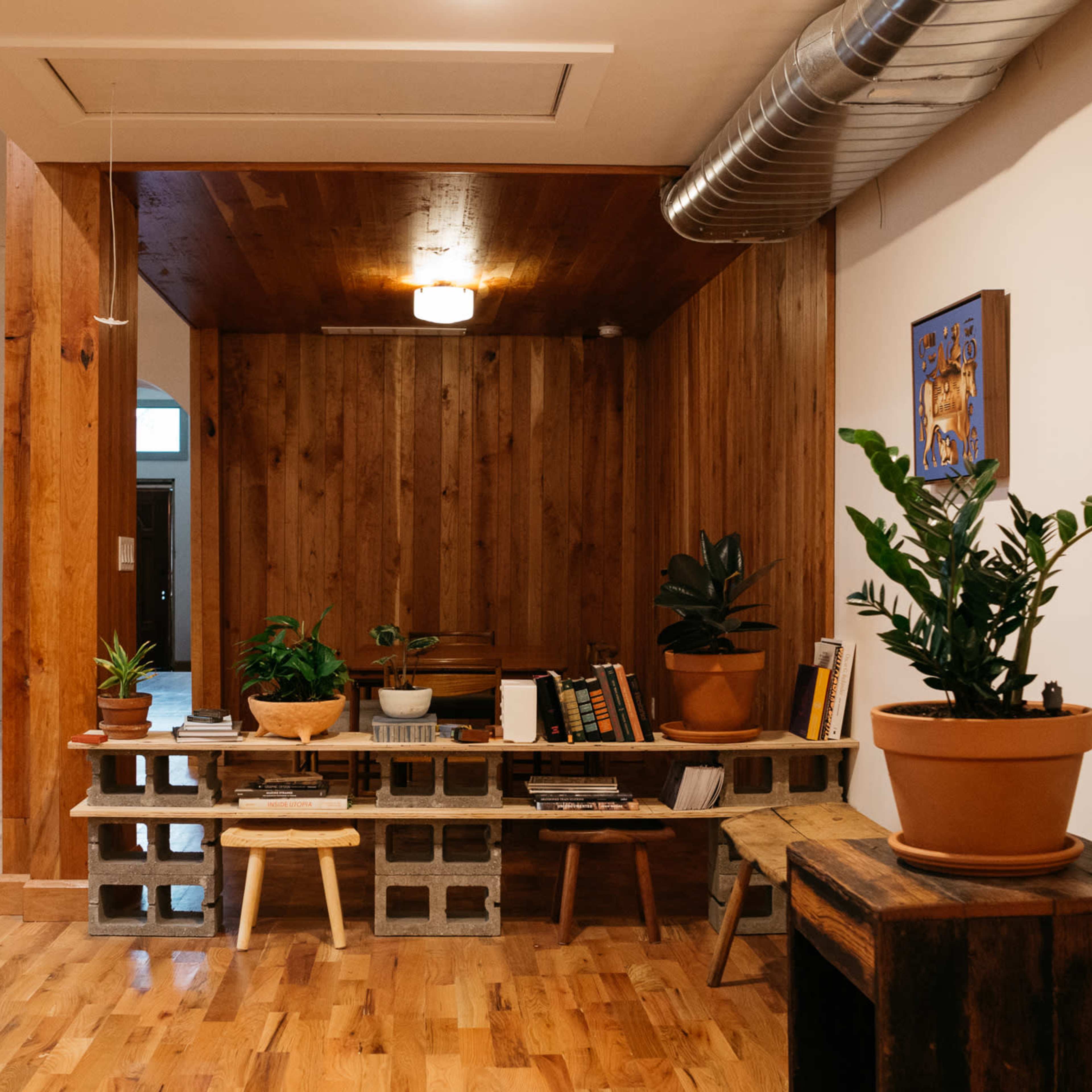 A modern interior space with wooden walls, a block furniture piece adorned with plants, and an open kitchen area in the background.