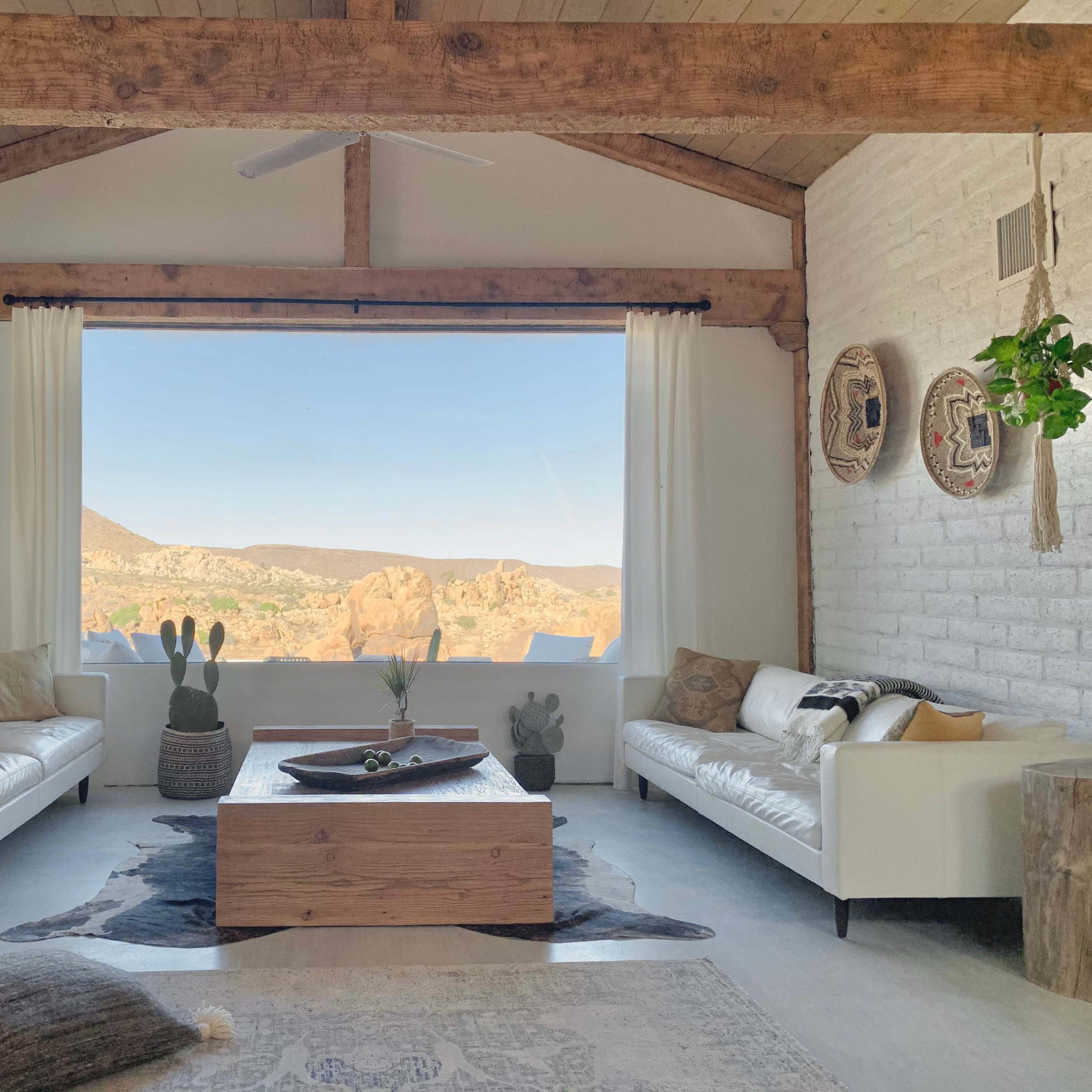 The living room features two white sofas facing a wooden coffee table, with large windows showcasing a mountainous landscape in the background.