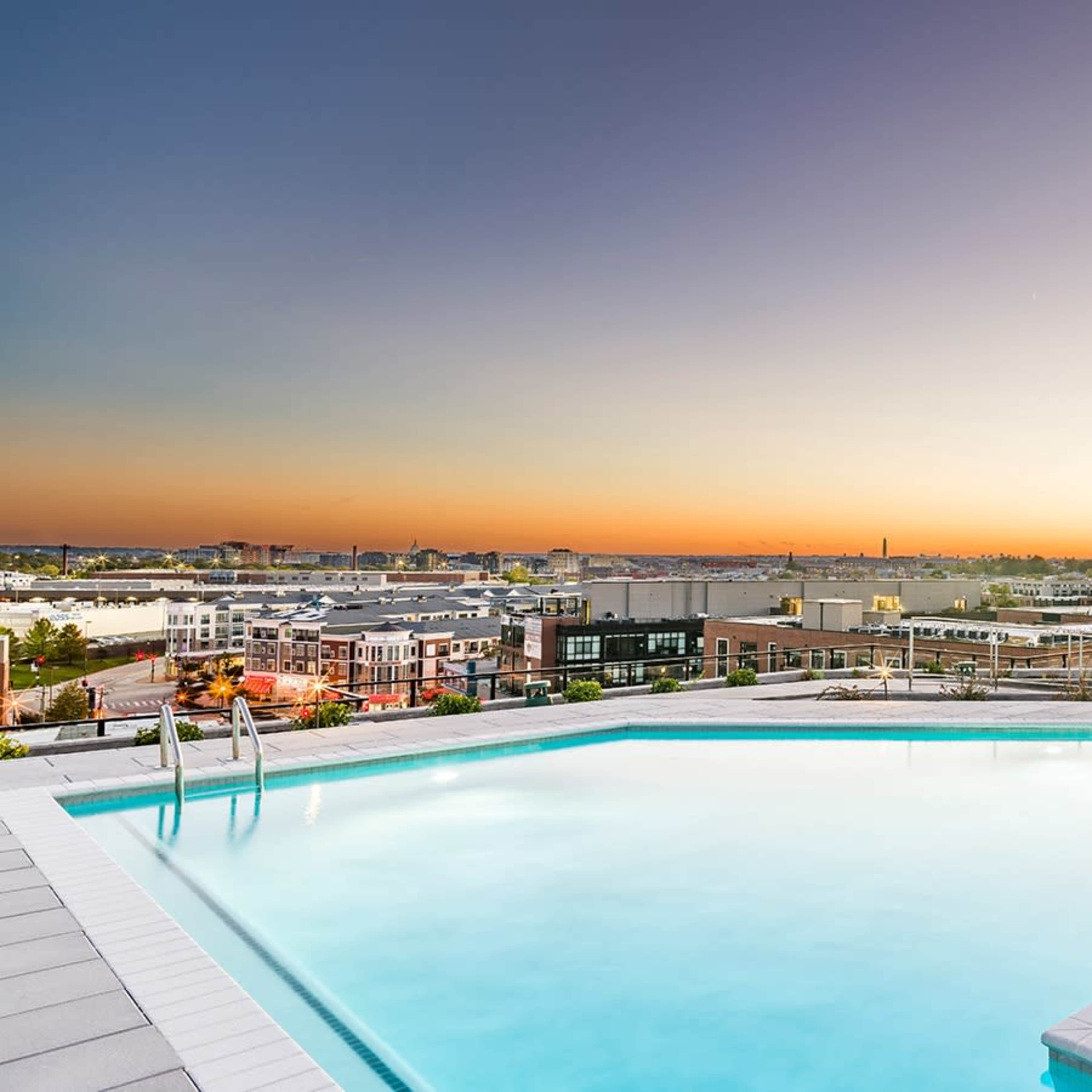 A rooftop pool reflects the colors of a sunset over a city skyline.