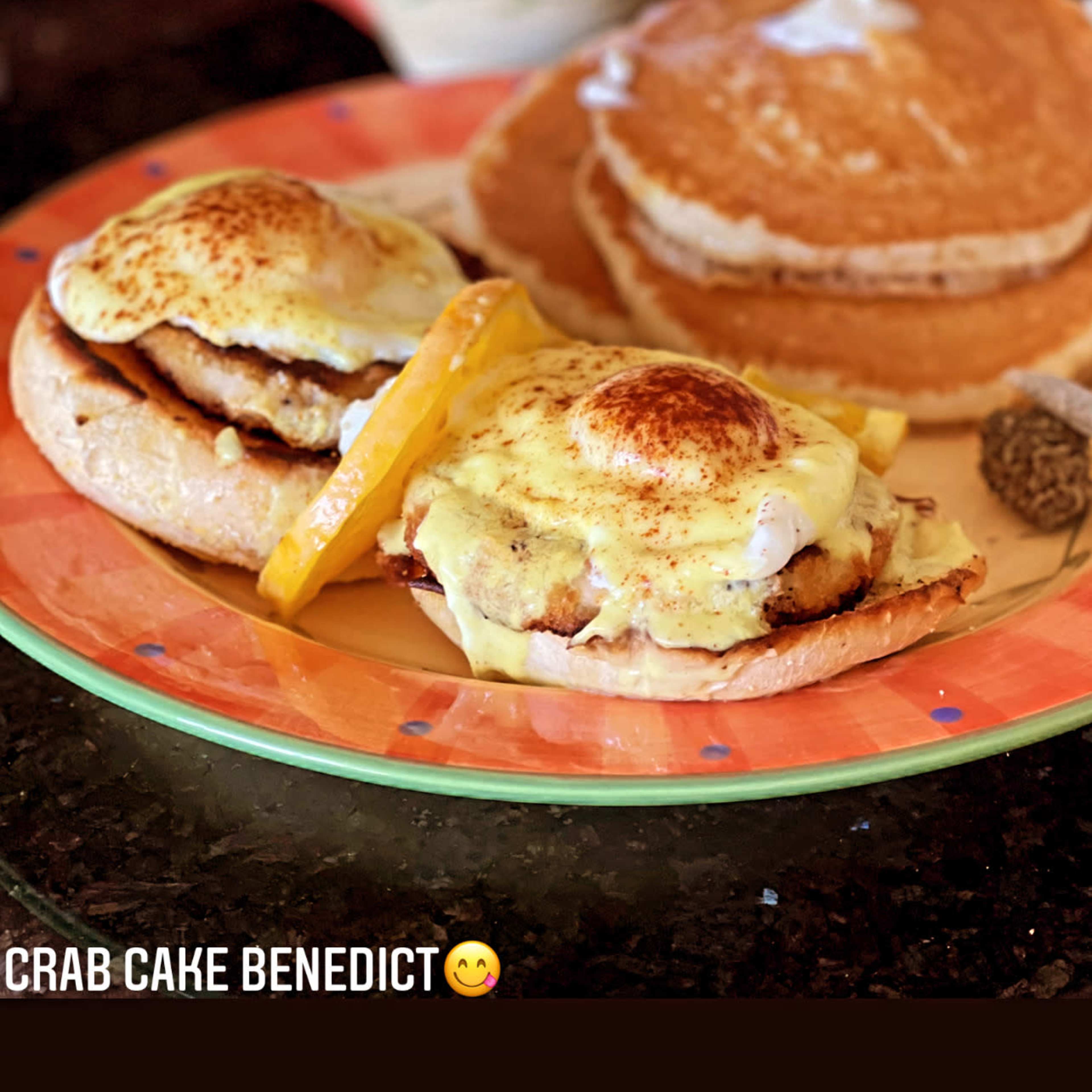 A plate of crab cake benedict with two portions on English muffins, a side of pancakes, and a cup of coffee.