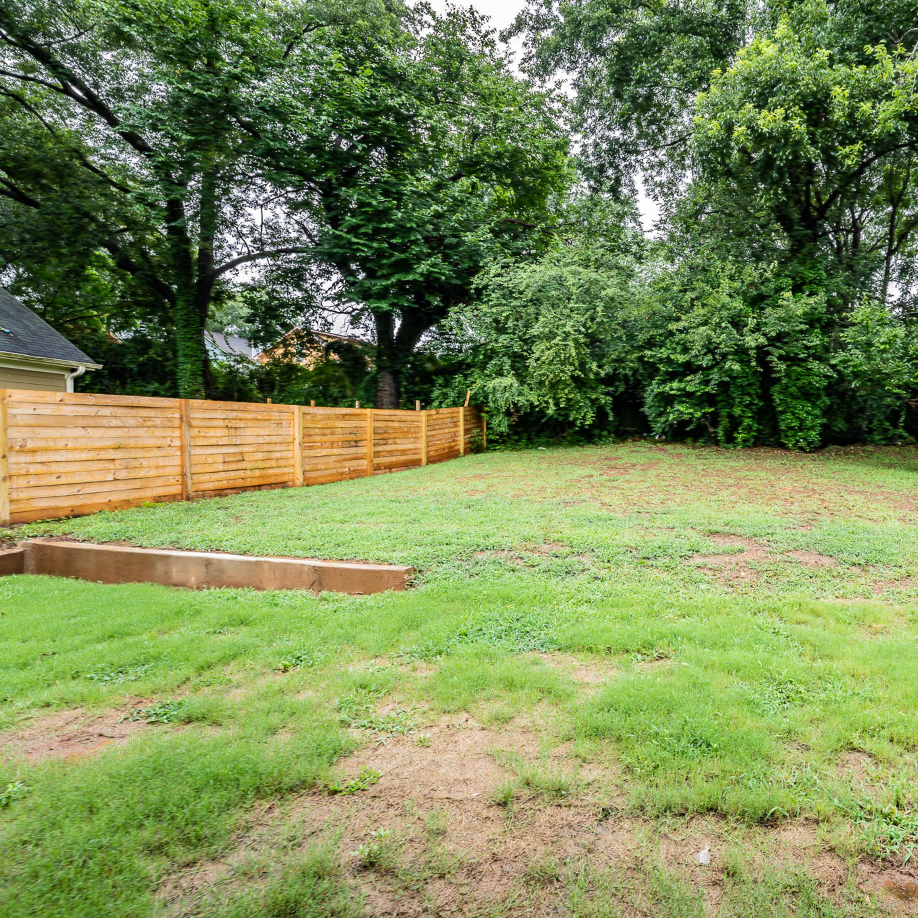 A grassy backyard with a wooden fence surrounds a wooded area.