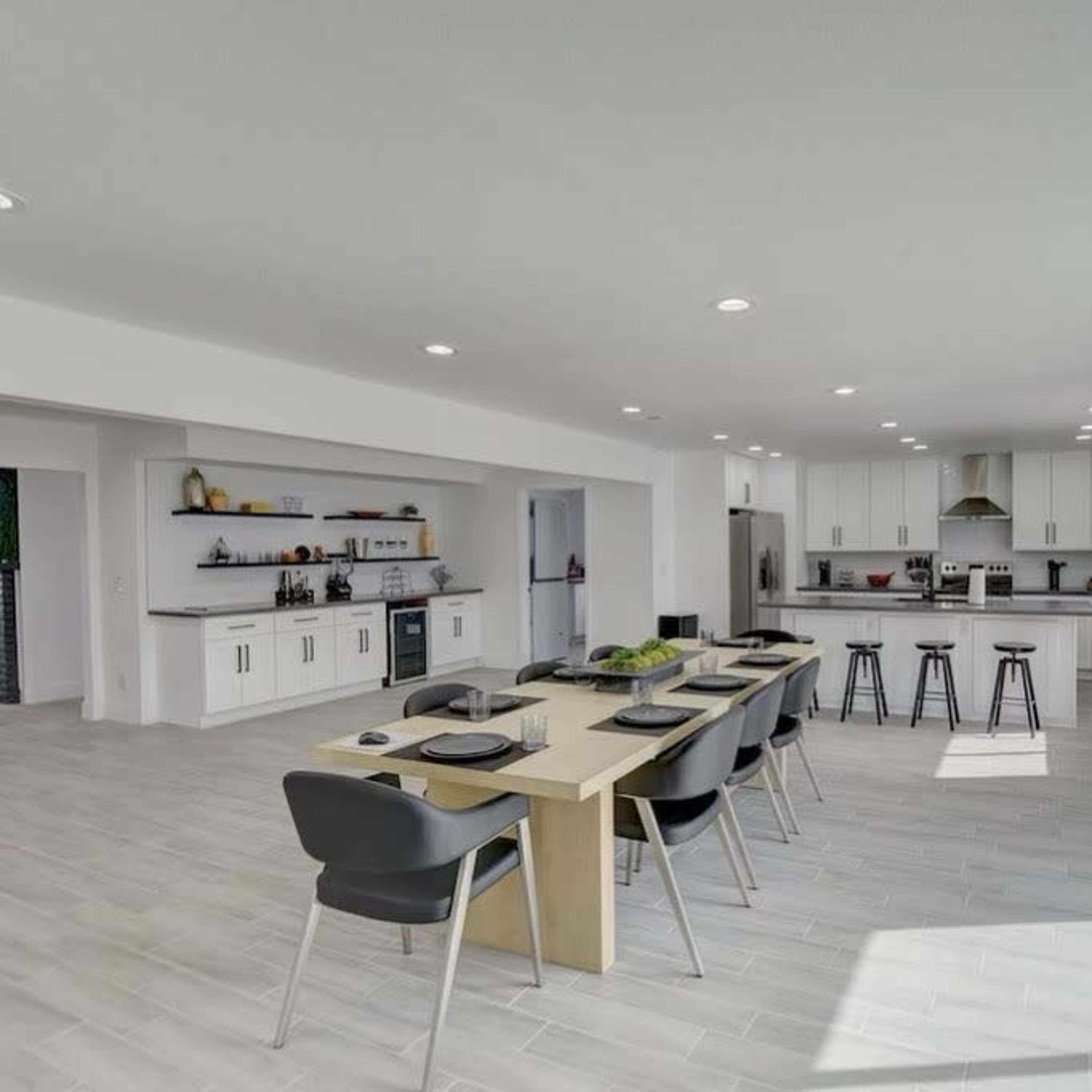 A modern kitchen features a large dining table, sleek cabinetry, and open space with natural light.