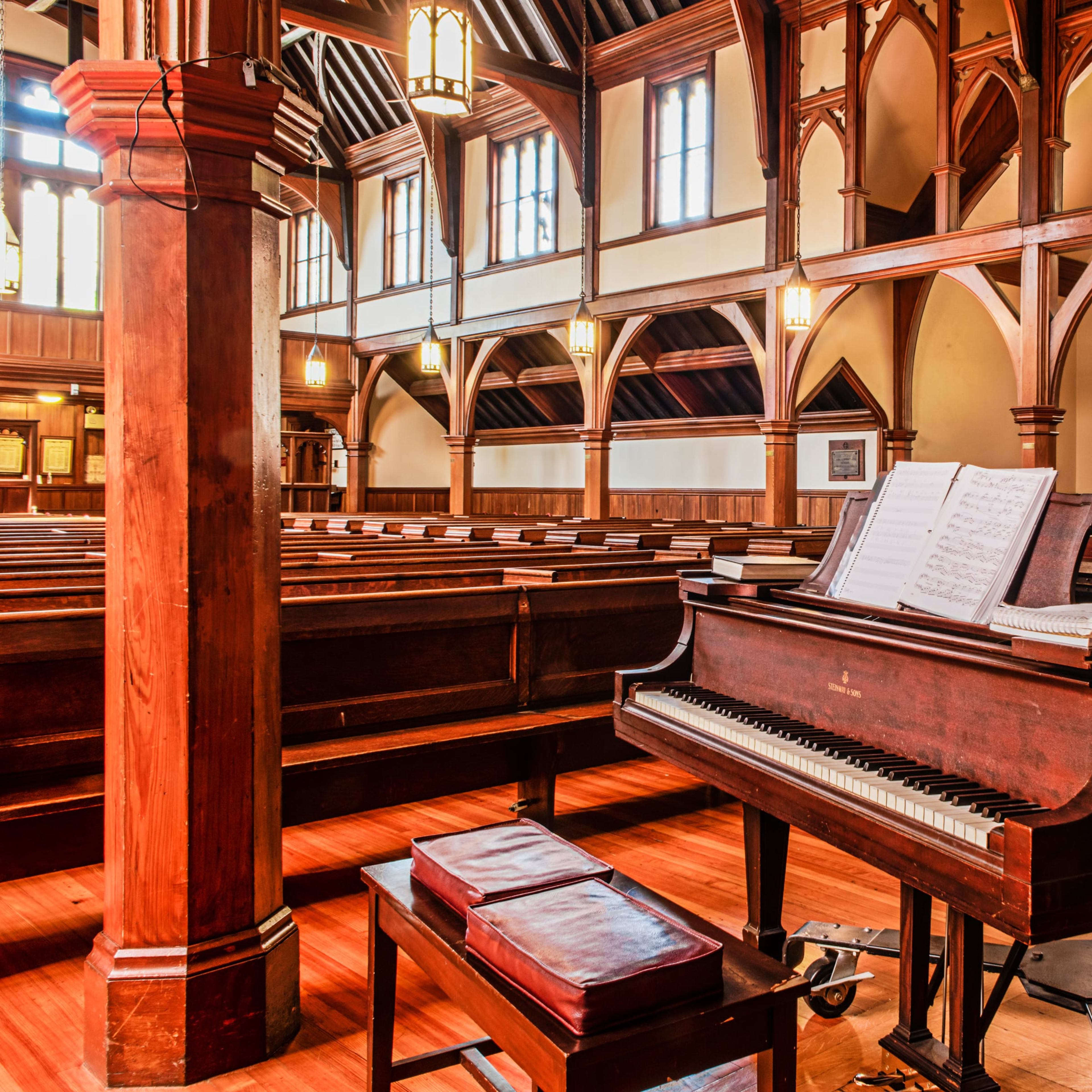 The interior of a church features wooden pews and a grand piano with sheet music, illuminated by stained glass windows.