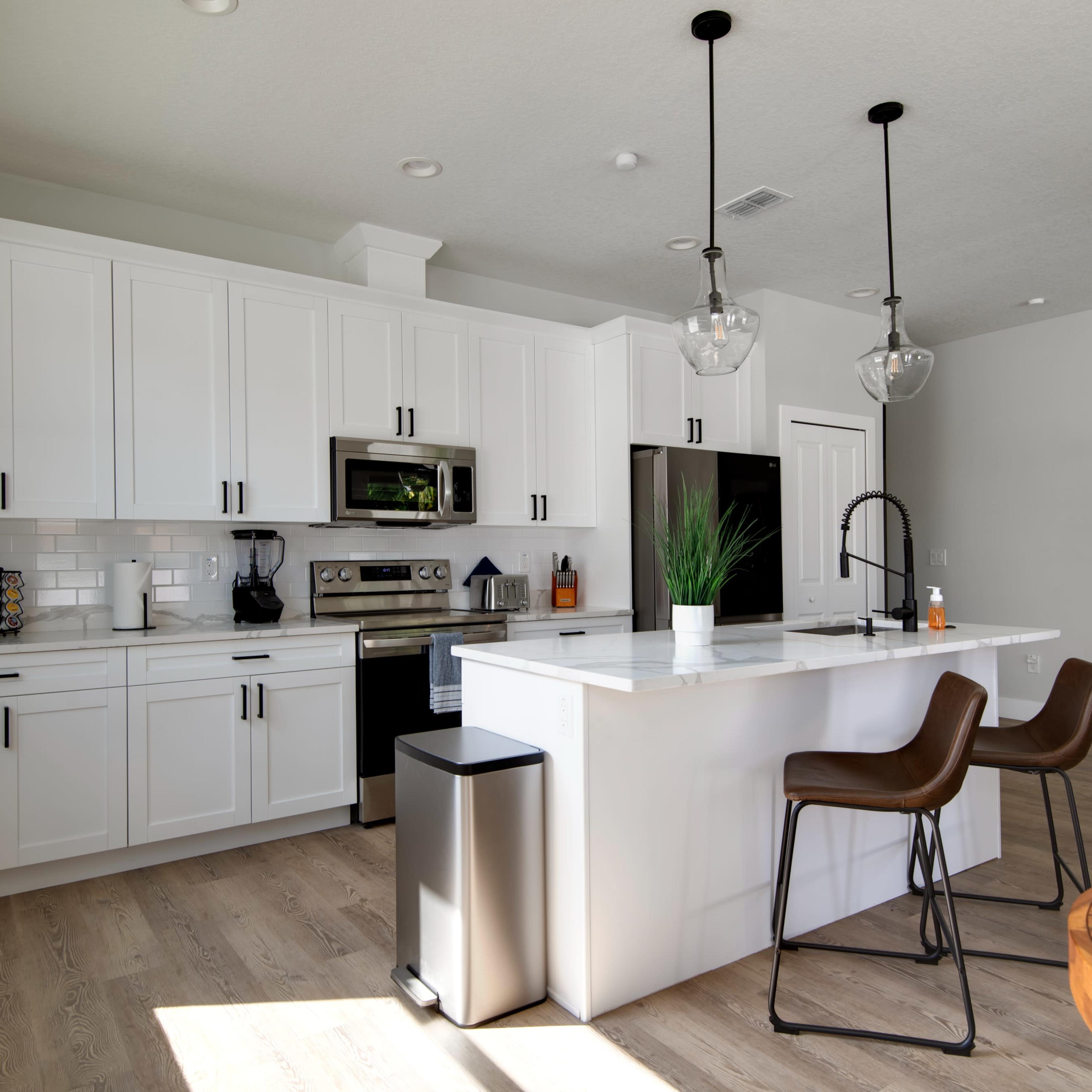 A modern kitchen features white cabinets, stainless steel appliances, and a large island with bar stools.