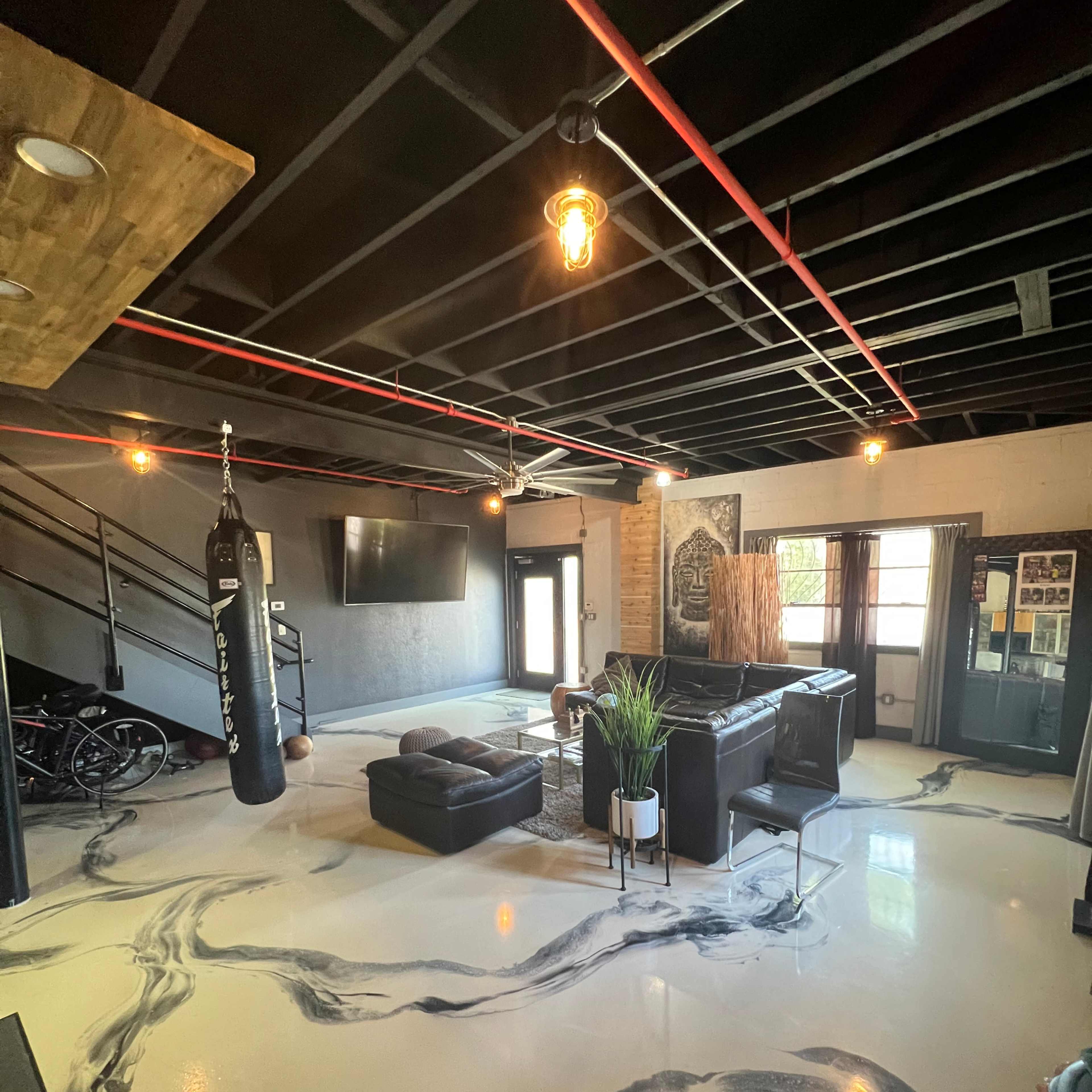 A modern interior space with black and white marbled flooring, a boxing bag hanging in one corner, and seating arranged around a central area with large windows.