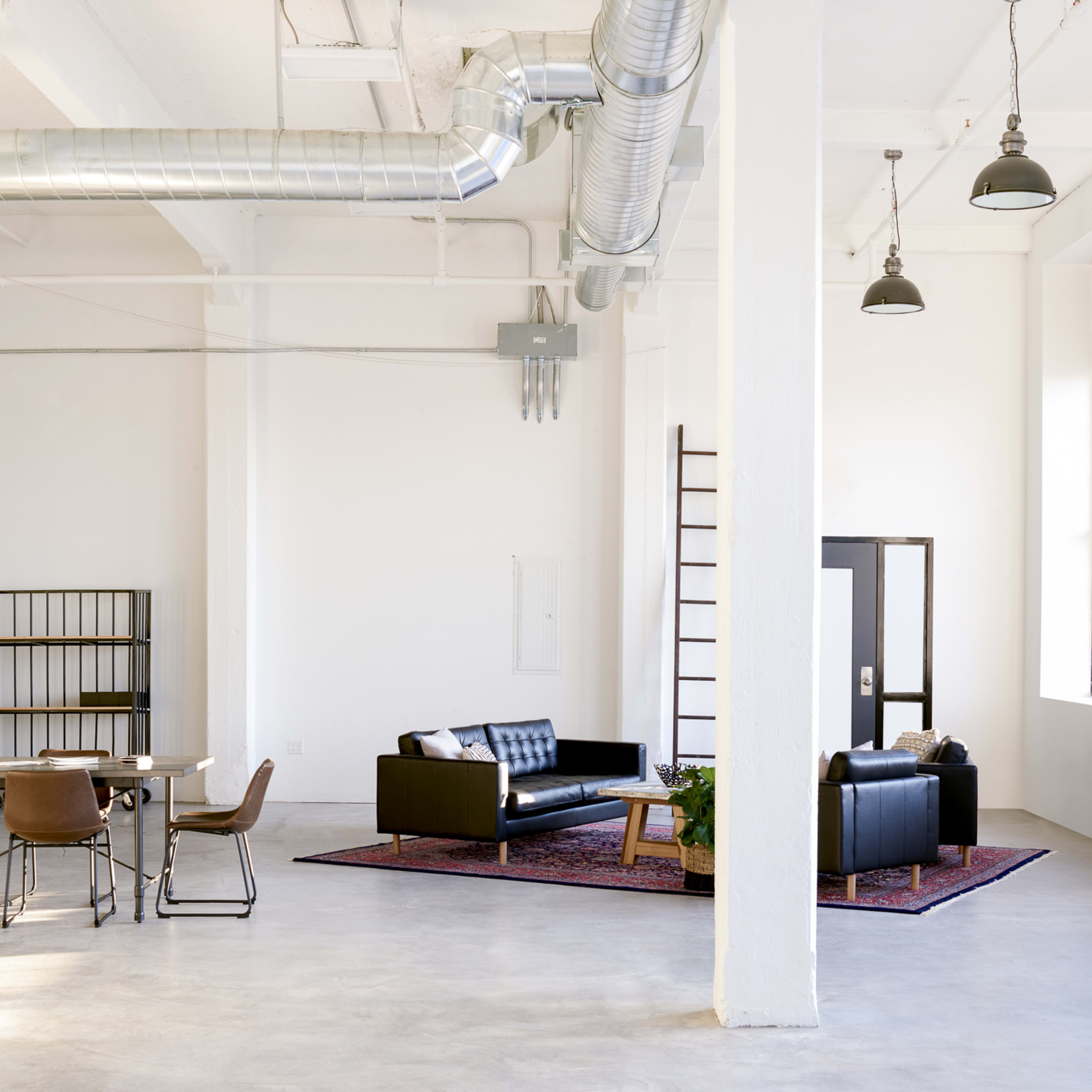 A spacious, modern room with a black sofa, a dining table, and industrial-style elements.