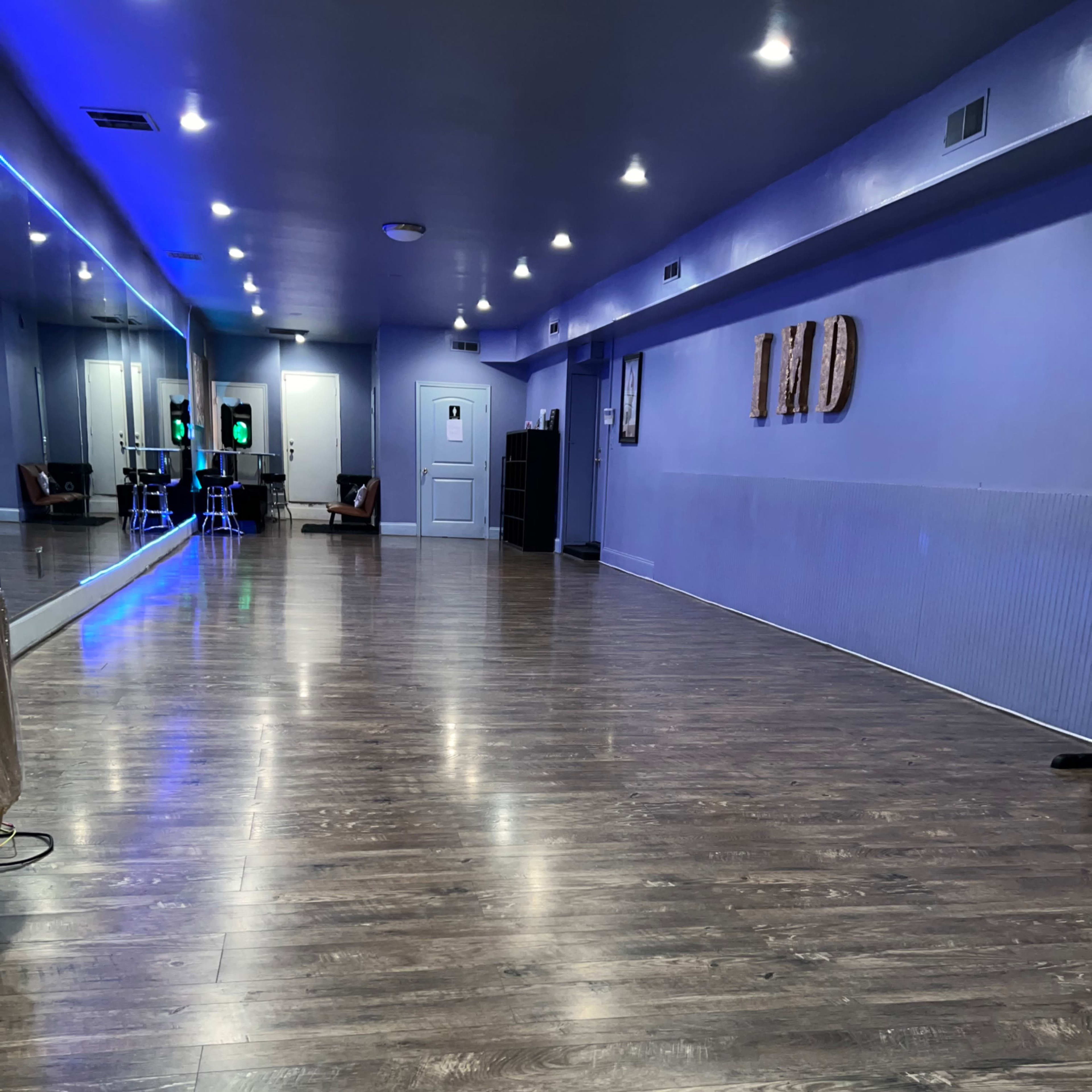 An empty dance studio with wooden flooring, mirrors along one wall, and ambient lighting.