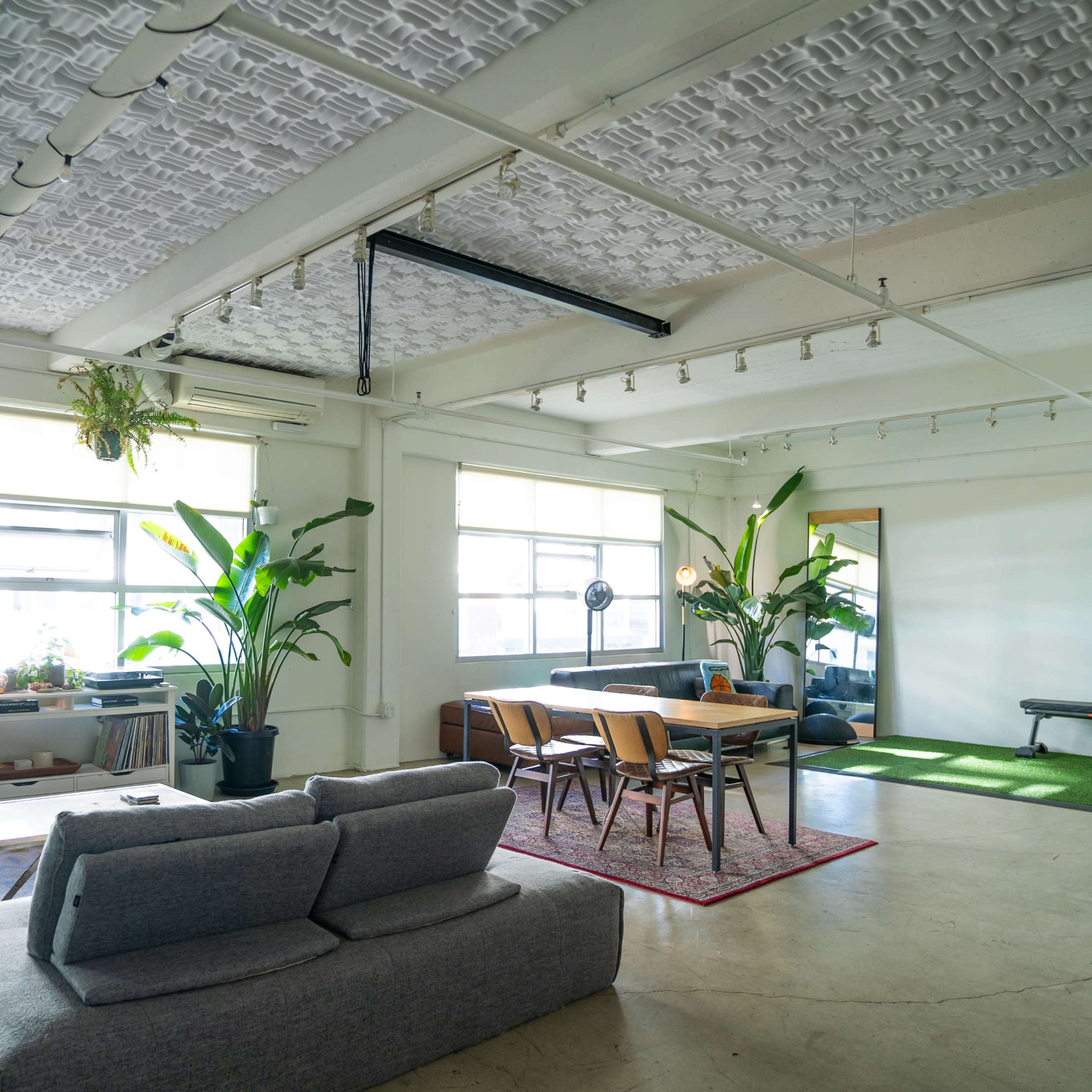 A spacious, modern living area featuring a seating area with gray sofas, a dining table with chairs, and large windows allowing natural light.