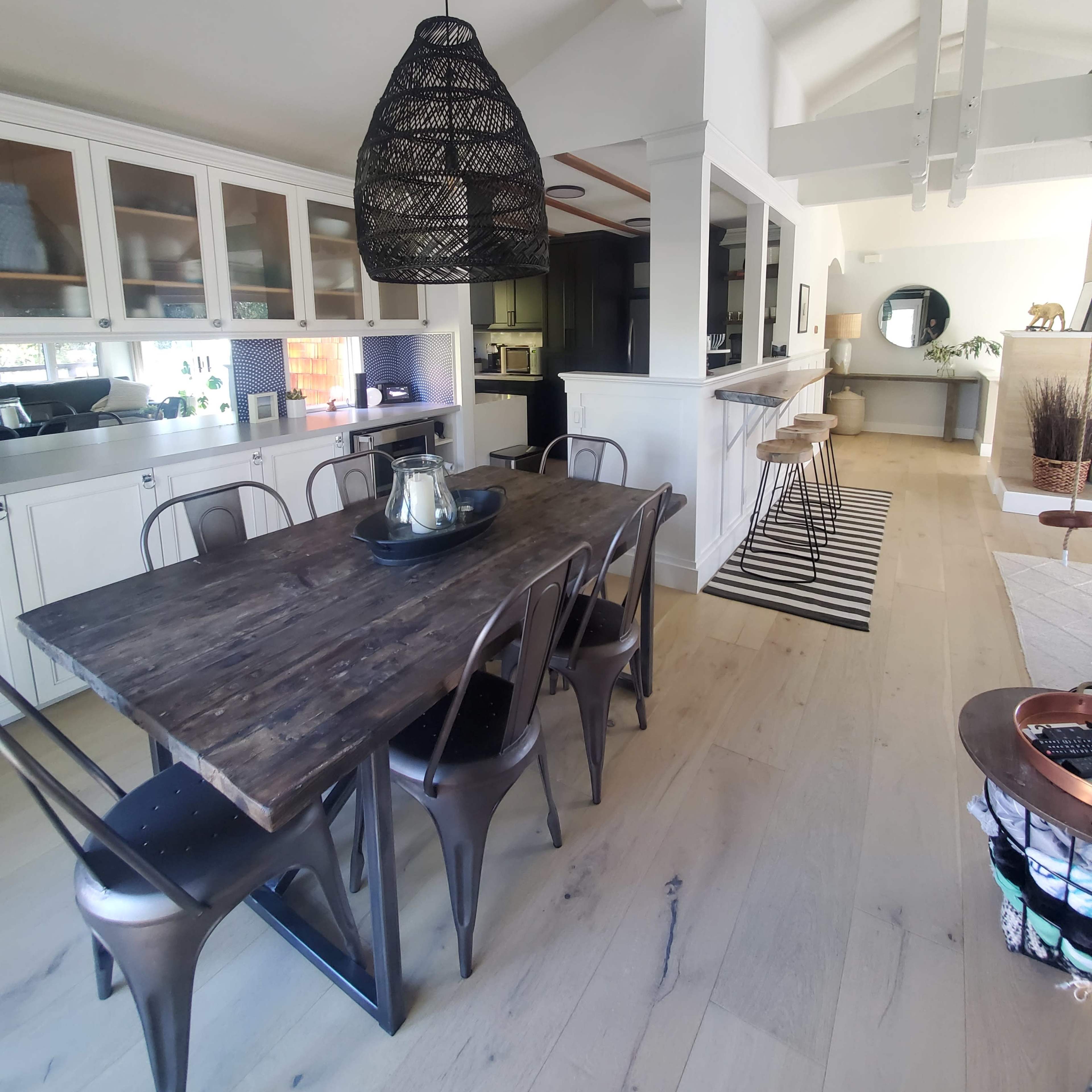 A modern kitchen and dining area with a wooden table surrounded by metal chairs, and a large pendant light hanging above.