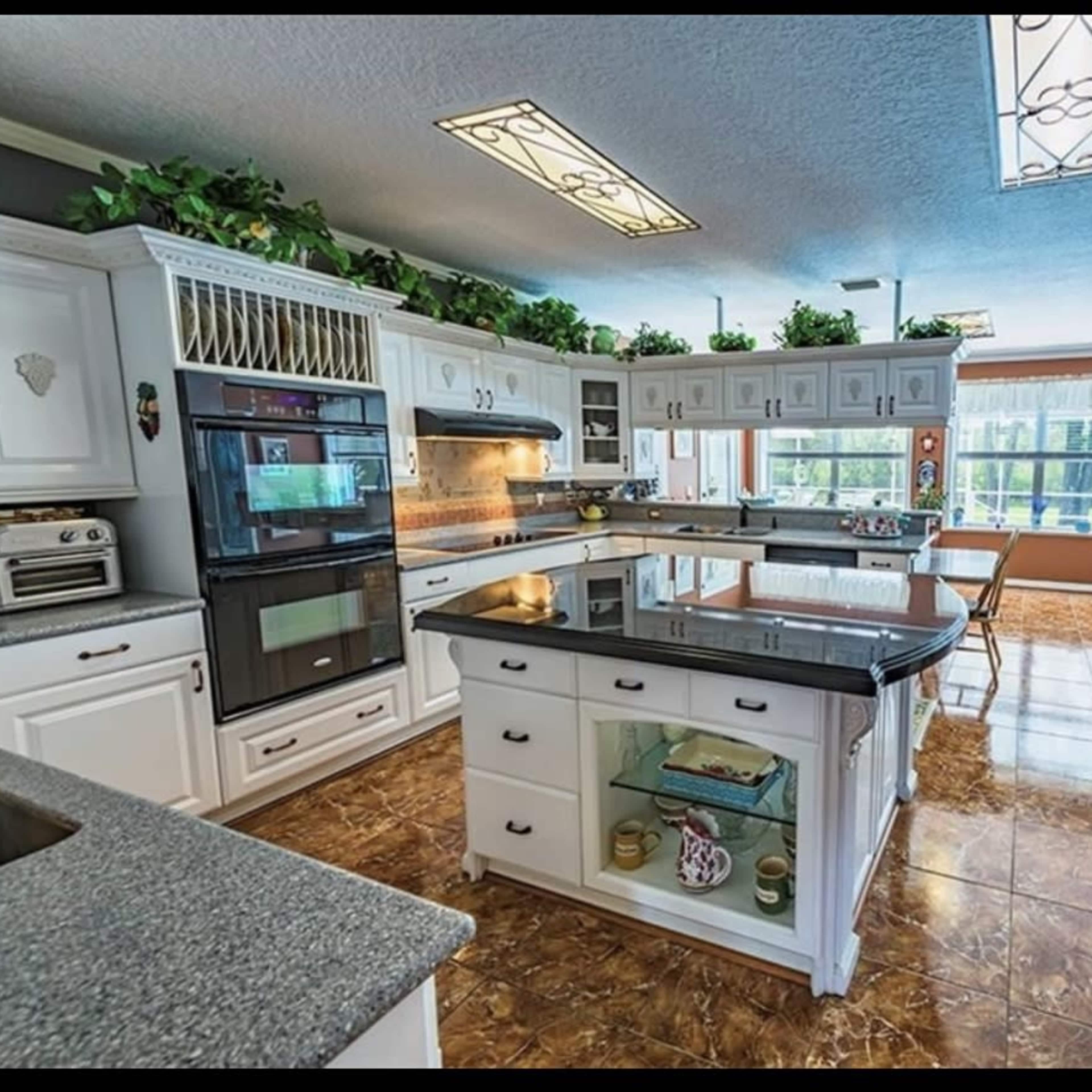 A spacious kitchen features white cabinetry, a central island with a black countertop, and large windows that allow natural light to fill the room.