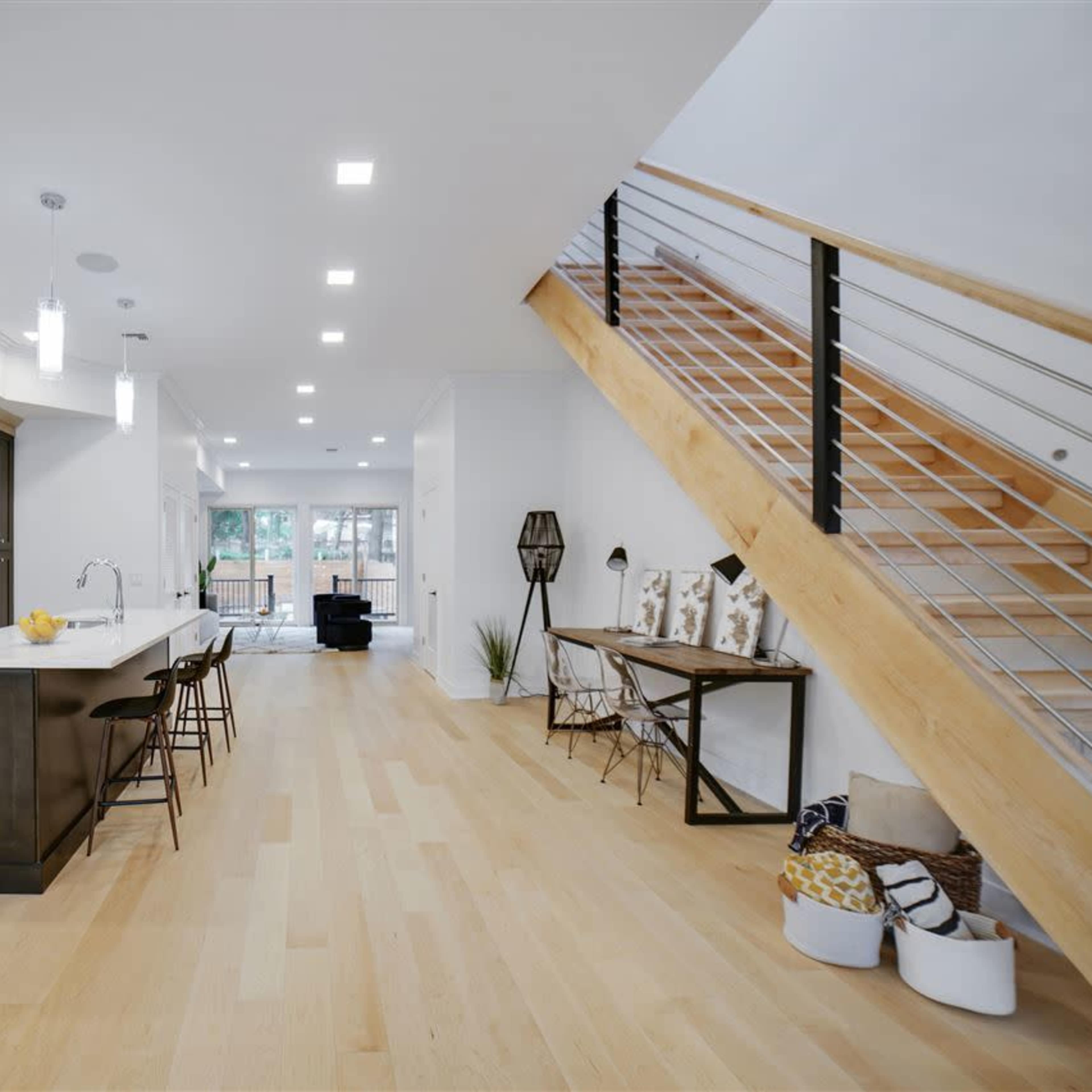 A modern kitchen with a kitchen island, stainless steel appliances, and a staircase leading to an upper level, with large windows allowing natural light.