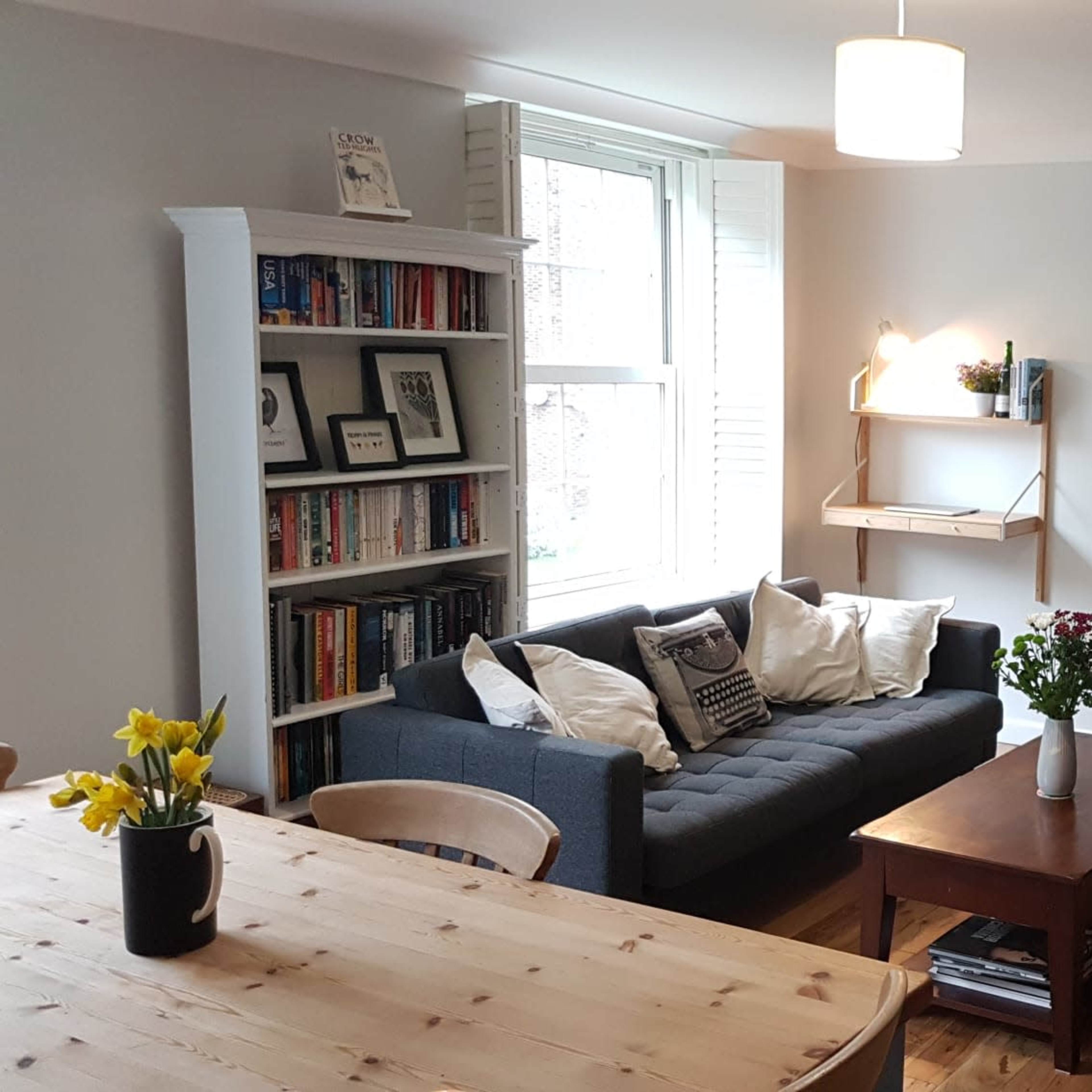 A cozy living room with a sofa, bookshelves filled with books, a wooden coffee table, and a dining area featuring a wooden table and chairs.
