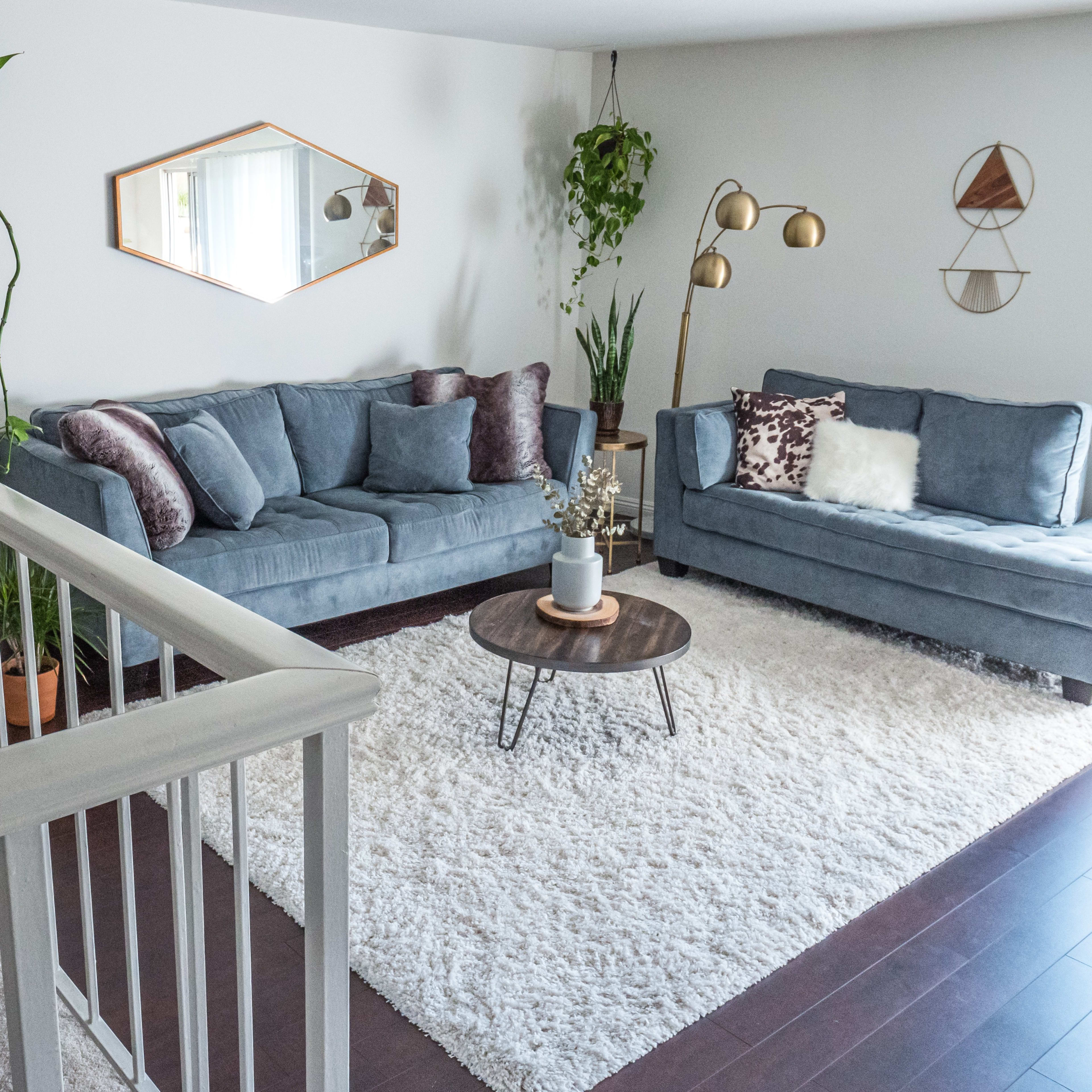 A modern living room features two blue sofas, a round coffee table, and decorative plants, arranged on a plush area rug.