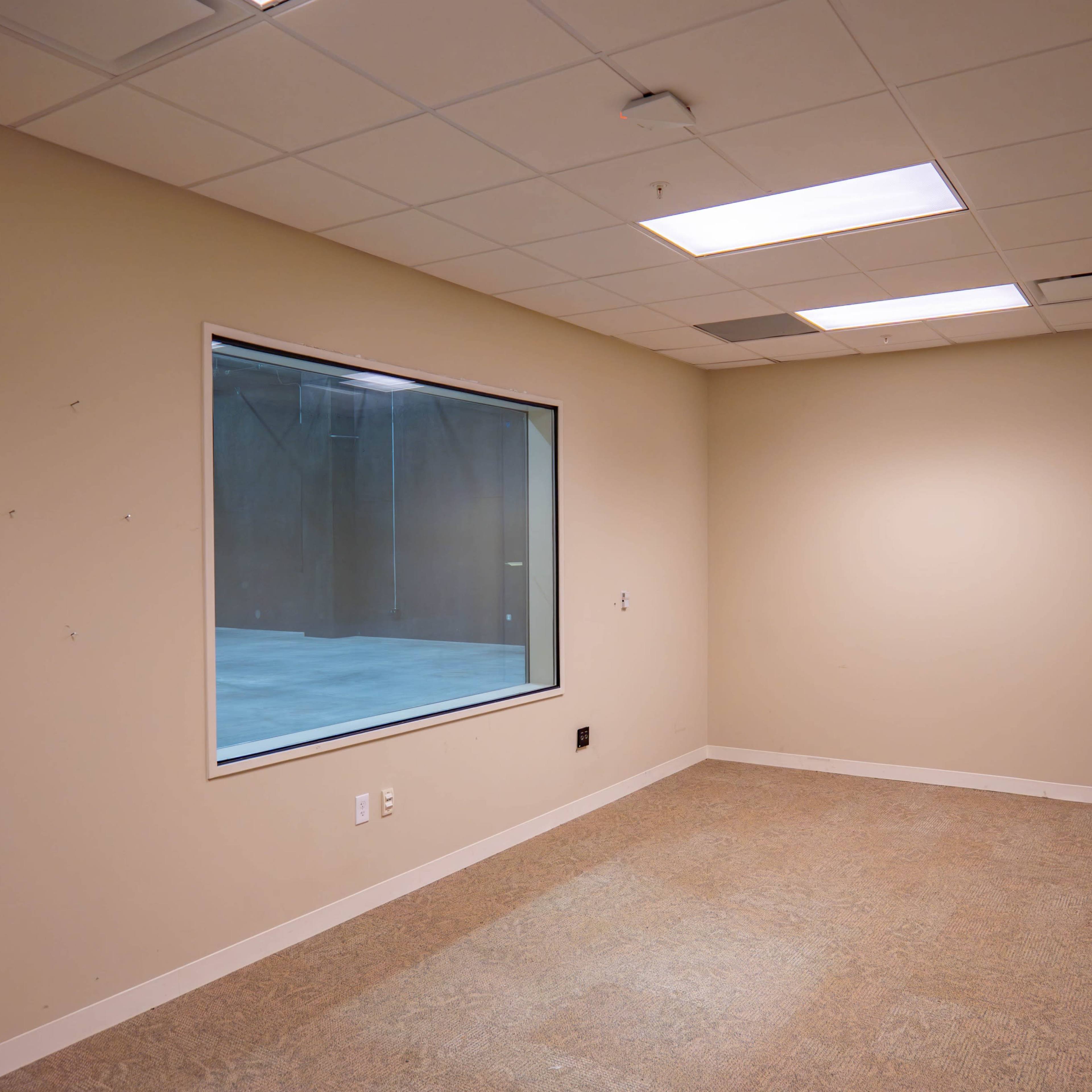 An empty room with a large window facing another room and a door on the left side.