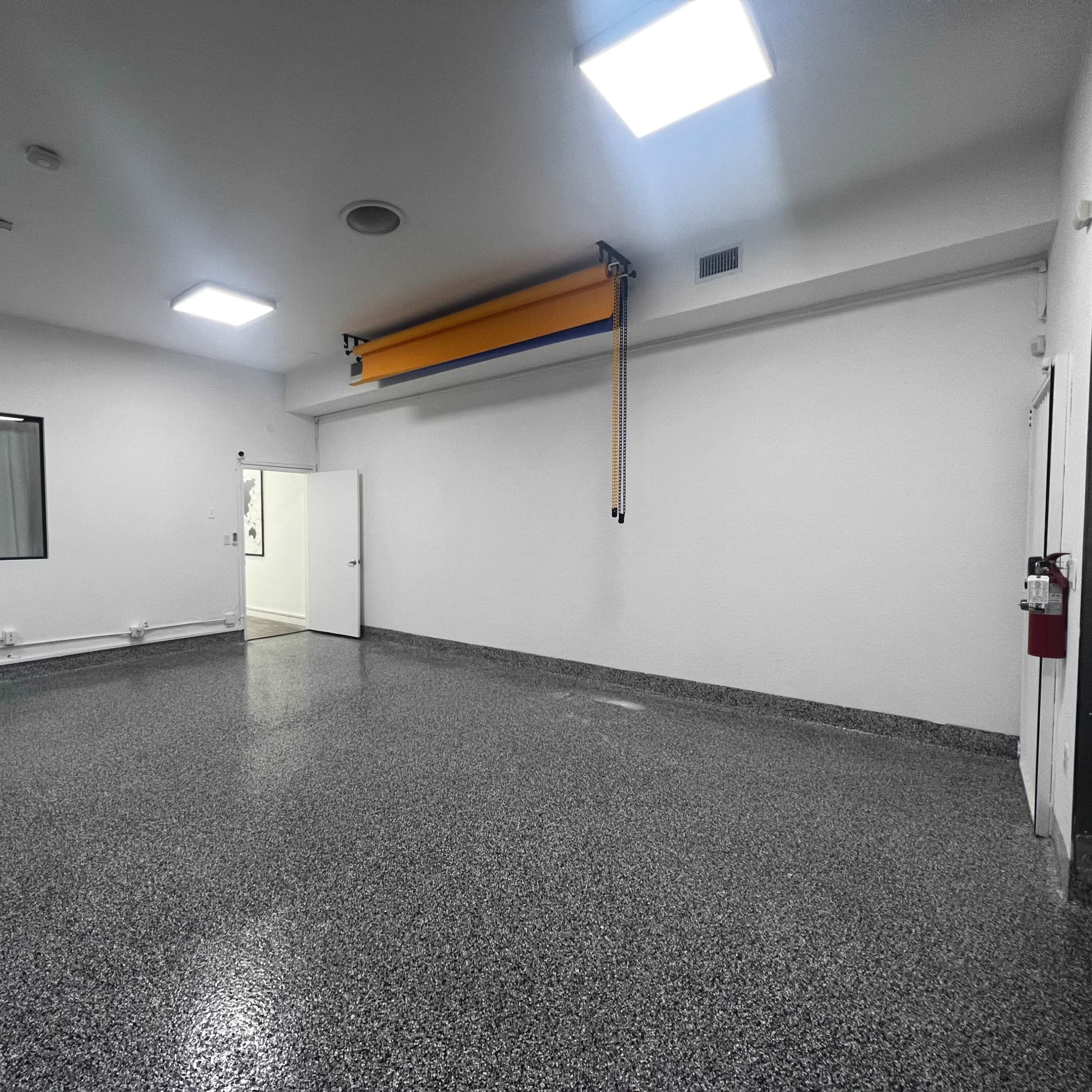 A spacious, empty room with a glossy floor, a large window covered by a curtain, and a door on one wall.